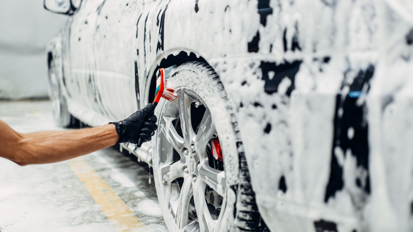Person washing a silver car with soap and a sponge in a car wash.