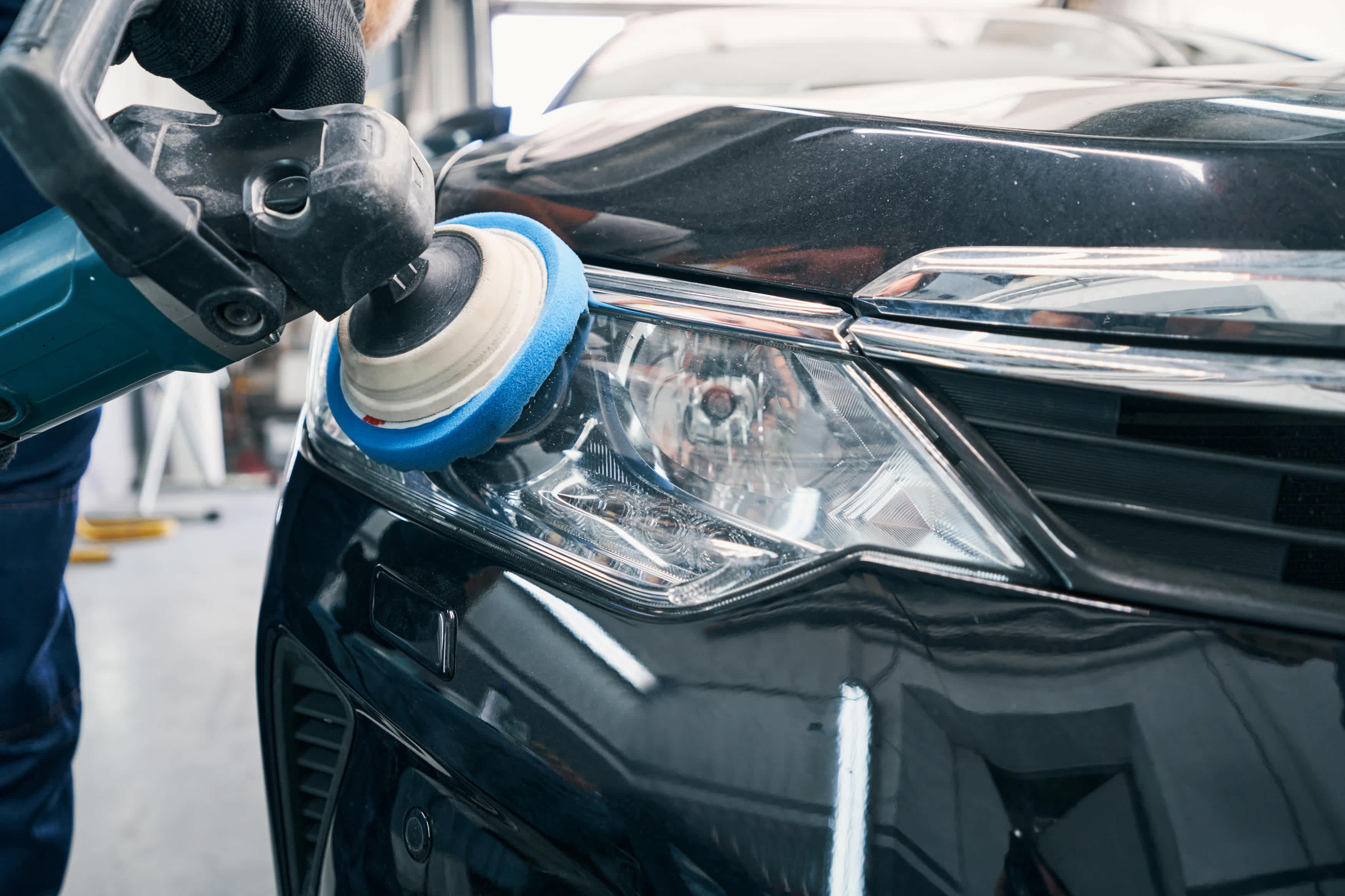 Person polishing the front of a black car with a circular buffer pad in a garage.