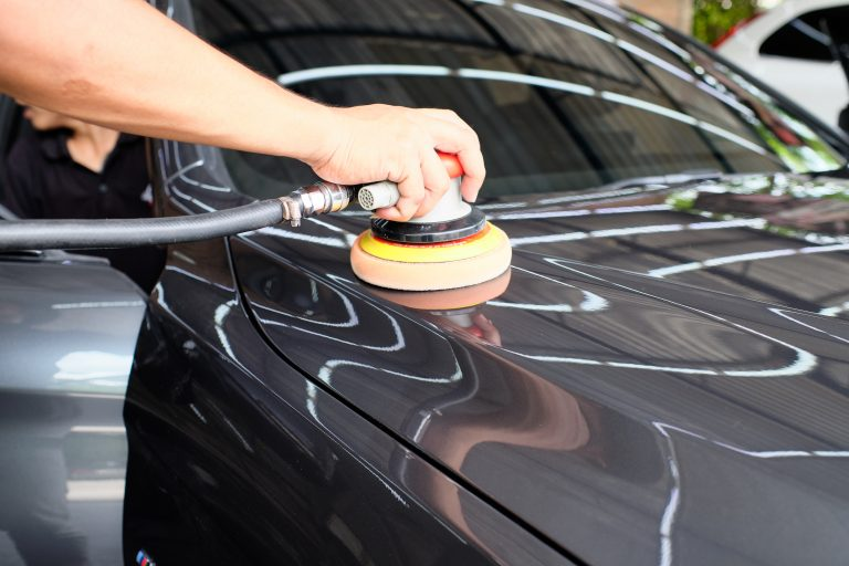 Person polishing a black car with a rotary buffer