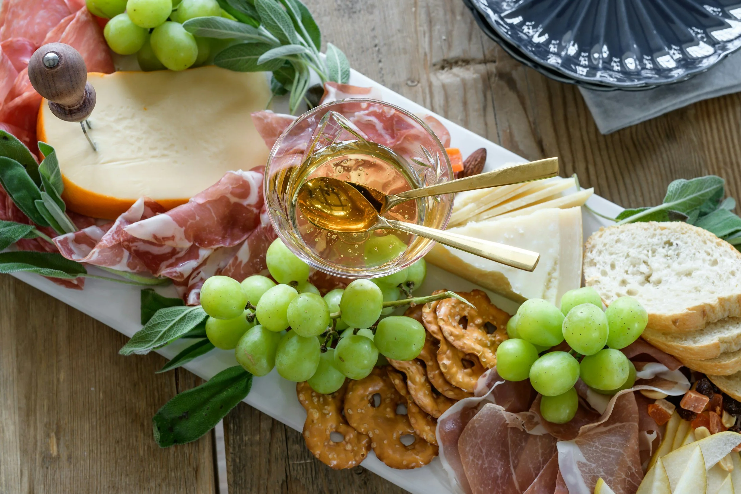 Charcuterie board with cheese, grapes, cracker, prosciutto, nuts, and a glass of white wine.