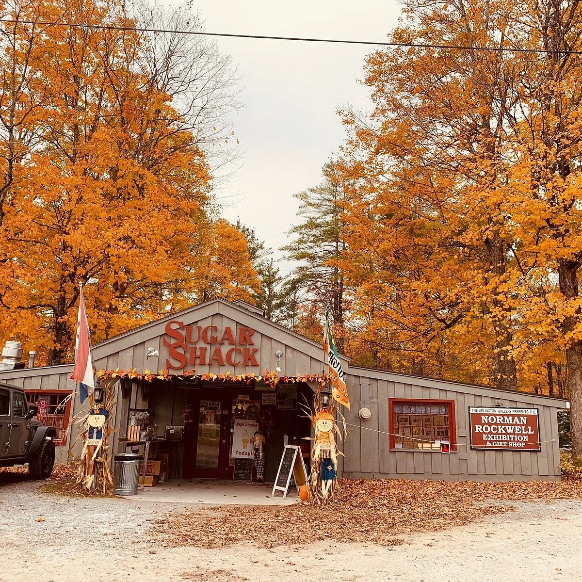 A small shop named Sugar Shack with fall decorations, surrounded by orange and yellow autumn trees.