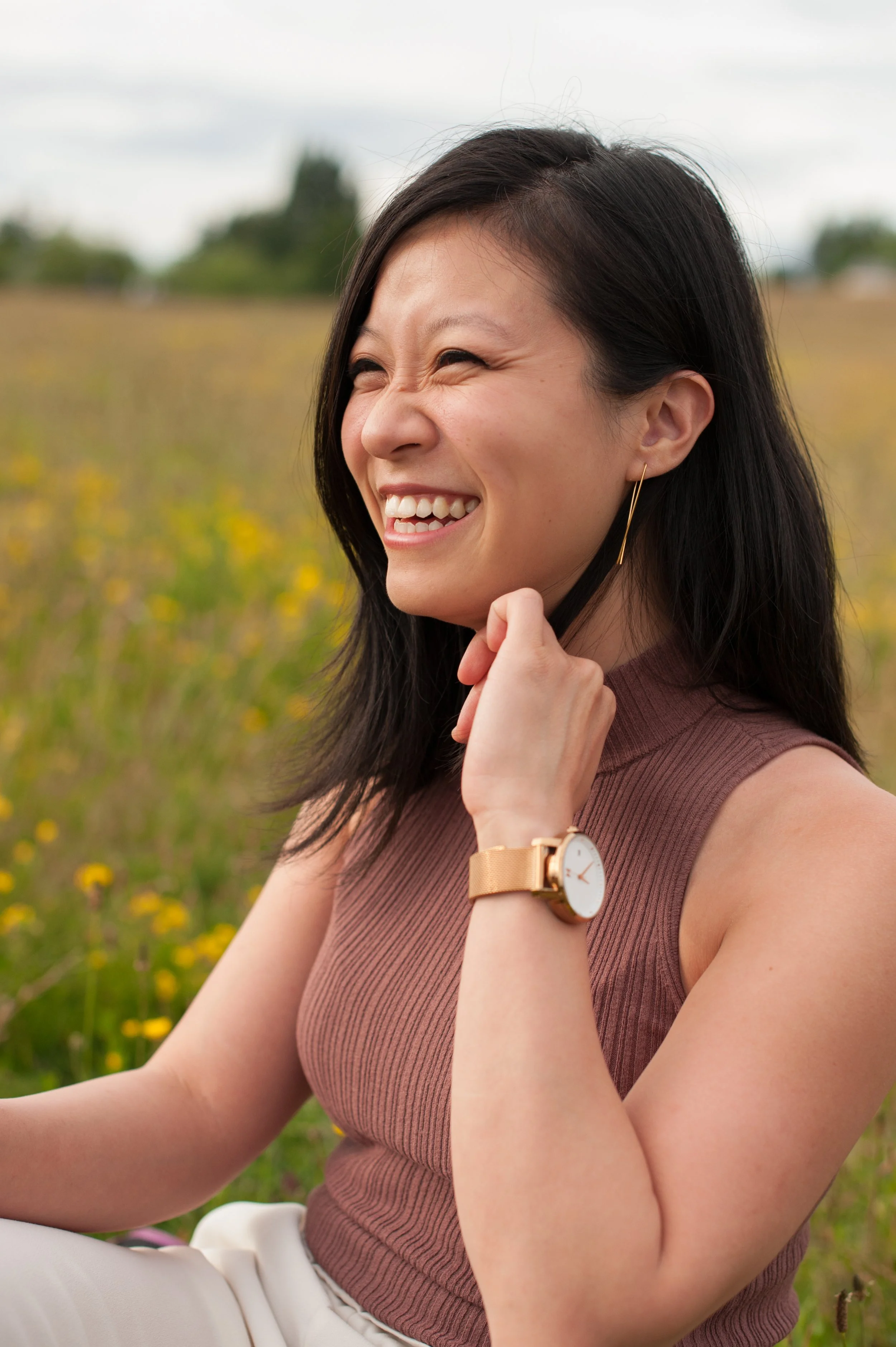 Founder of Authenticity Unearthed laughing joyfully outdoors in a sunny wildflowerfield, wearing a mauve sleeveless top and gold watch