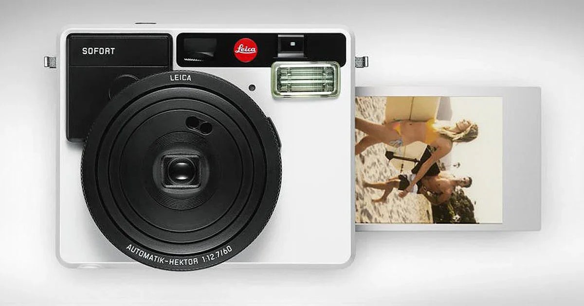 A vintage Leica camera with a small photo card attached, showing two women on the beach, one with a brown swimsuit and the other with a black bikini.