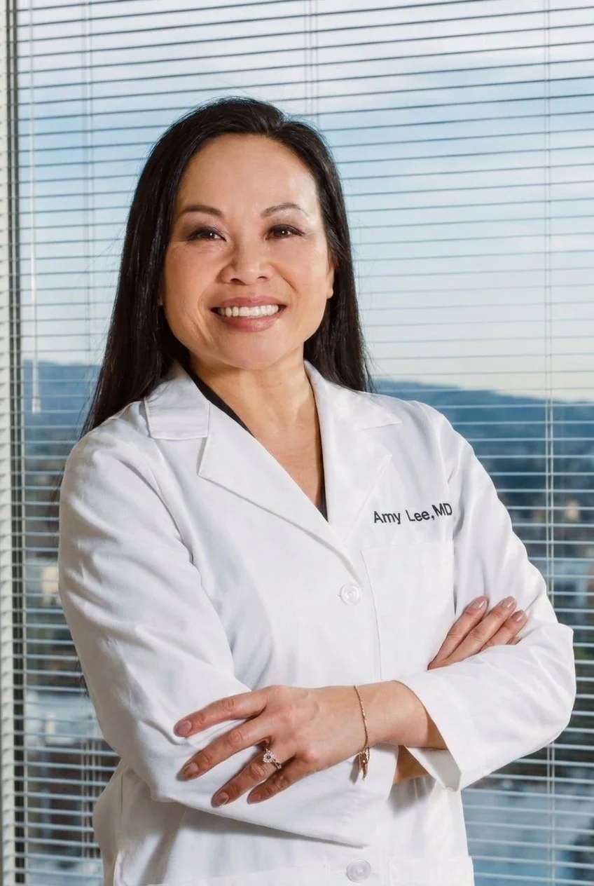 A smiling woman wearing a white medical coat with the name tag 'Amy Lee, MD' standing in front of a window with blinds.