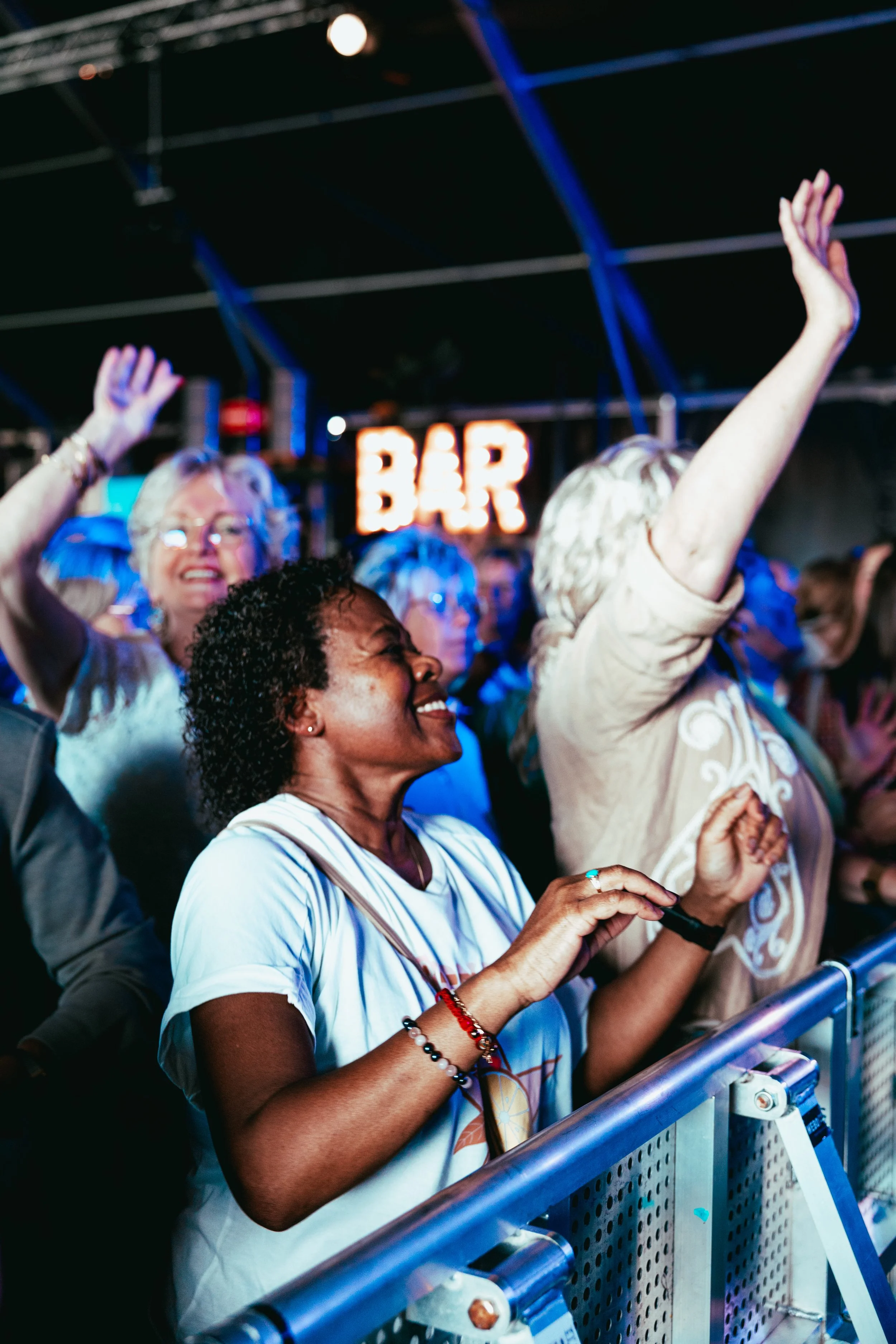 People enjoying live music performance at a concert, with some raising their hands and smiling.