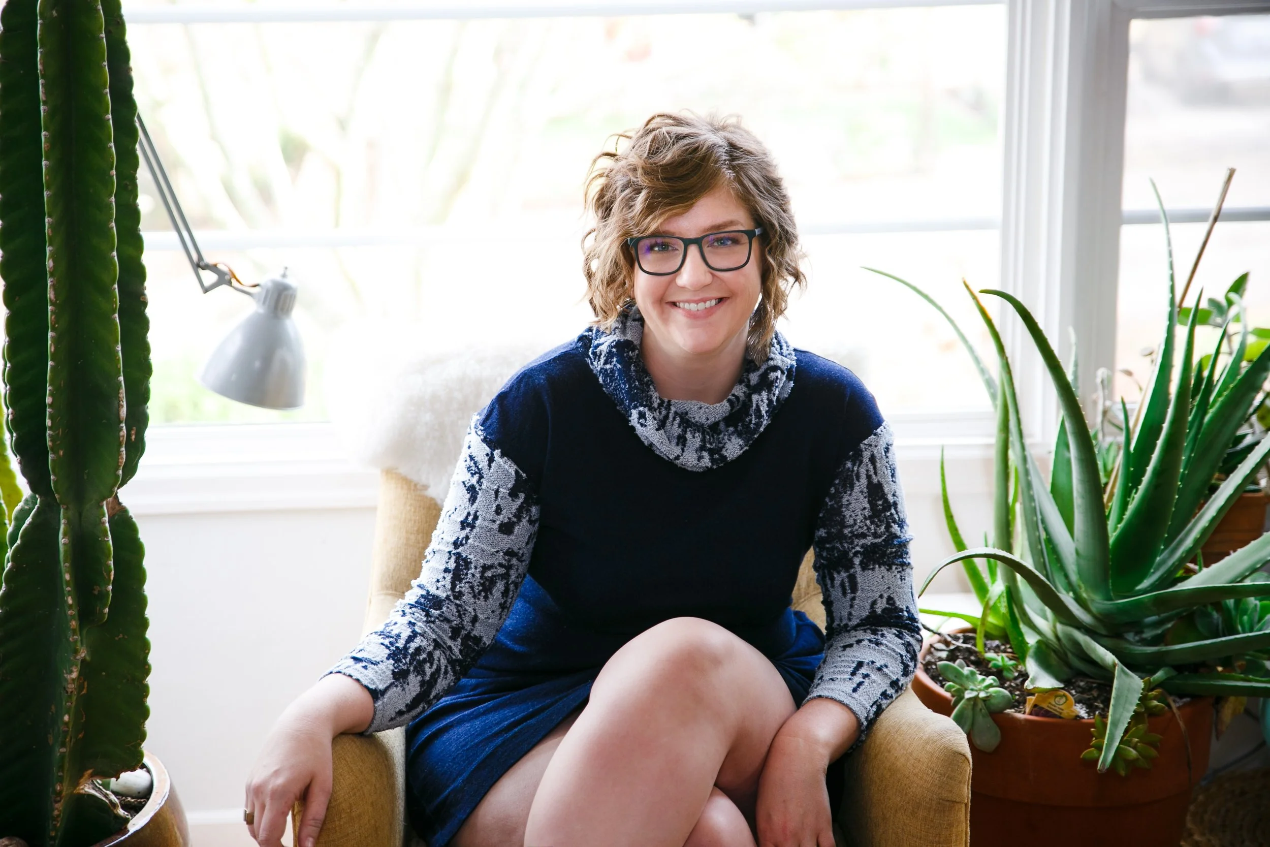 Portrait of Kim, a white woman with glasses, with her plant collection.