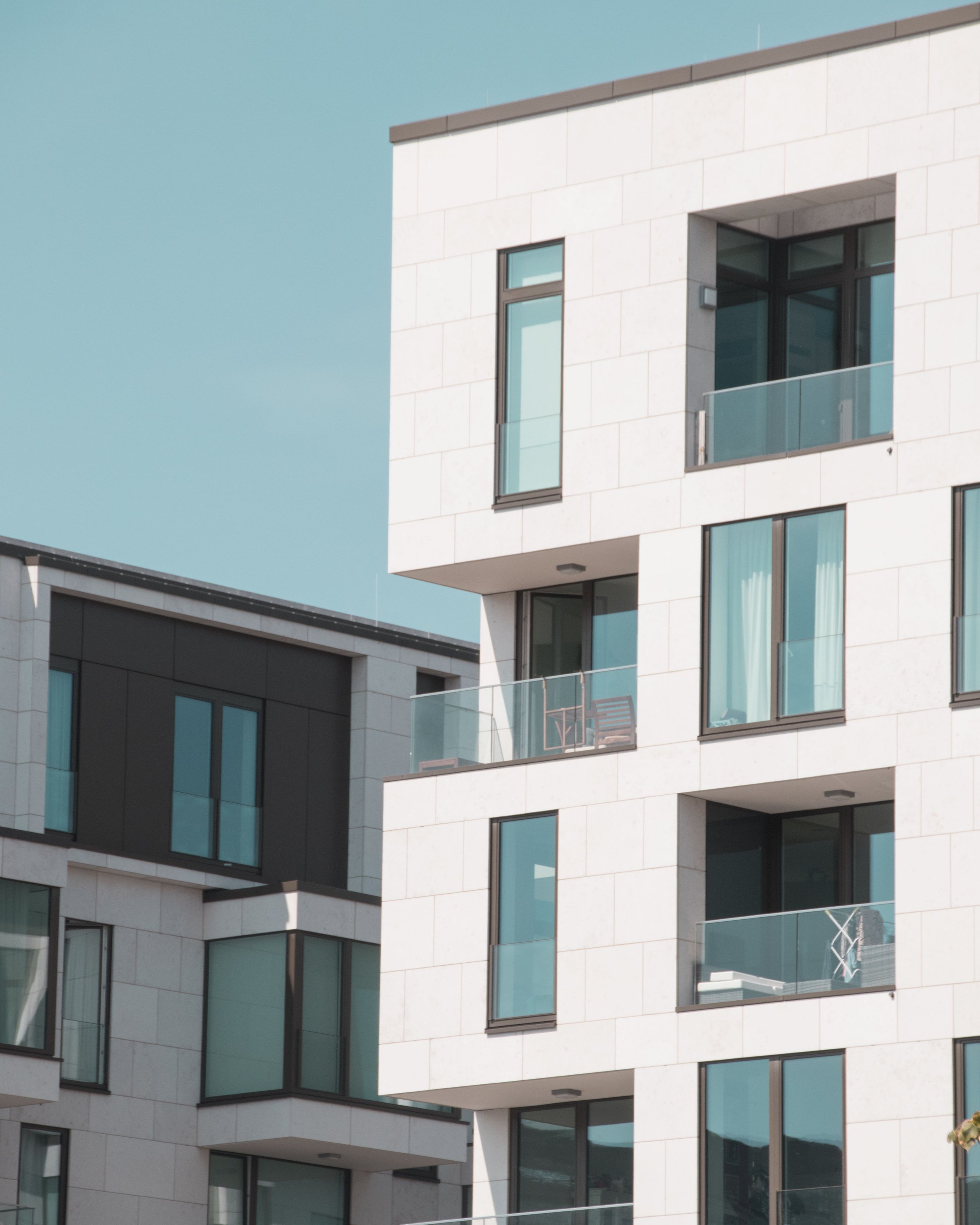 Modern white apartment building with large glass windows and balconies, against a clear blue sky.
