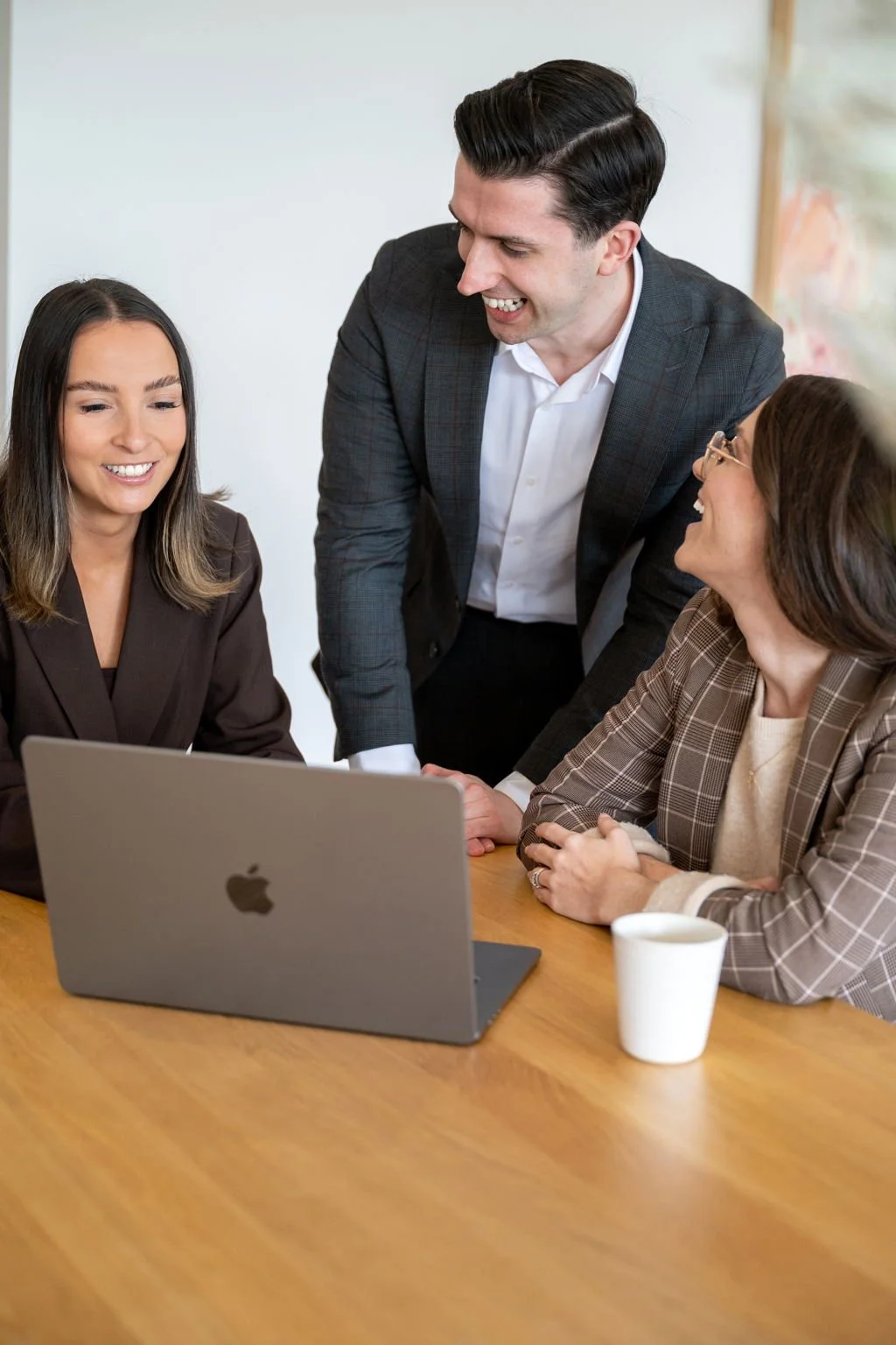 Four colleagues gathered around a laptop during a meeting, smiling and engaging.