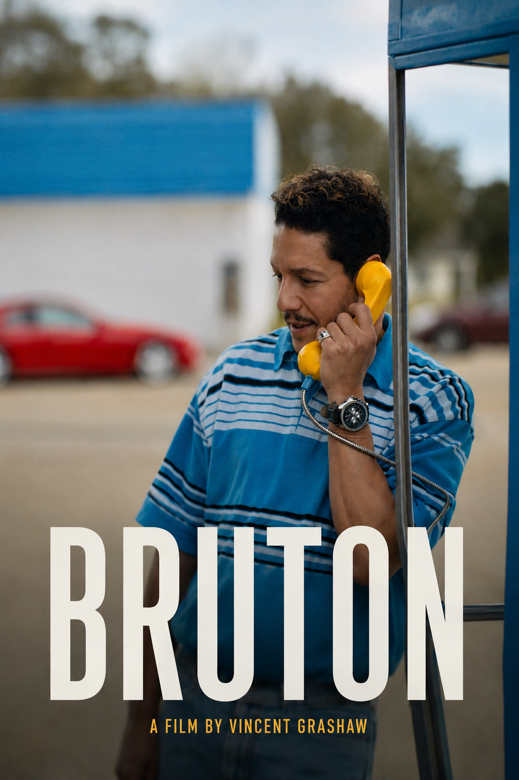 A man with curly brown hair, wearing a blue striped shirt and a large watch, is talking on a yellow payphone.