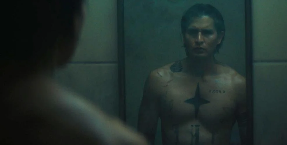 A woman with tattoos looking at her reflection in a mirror.