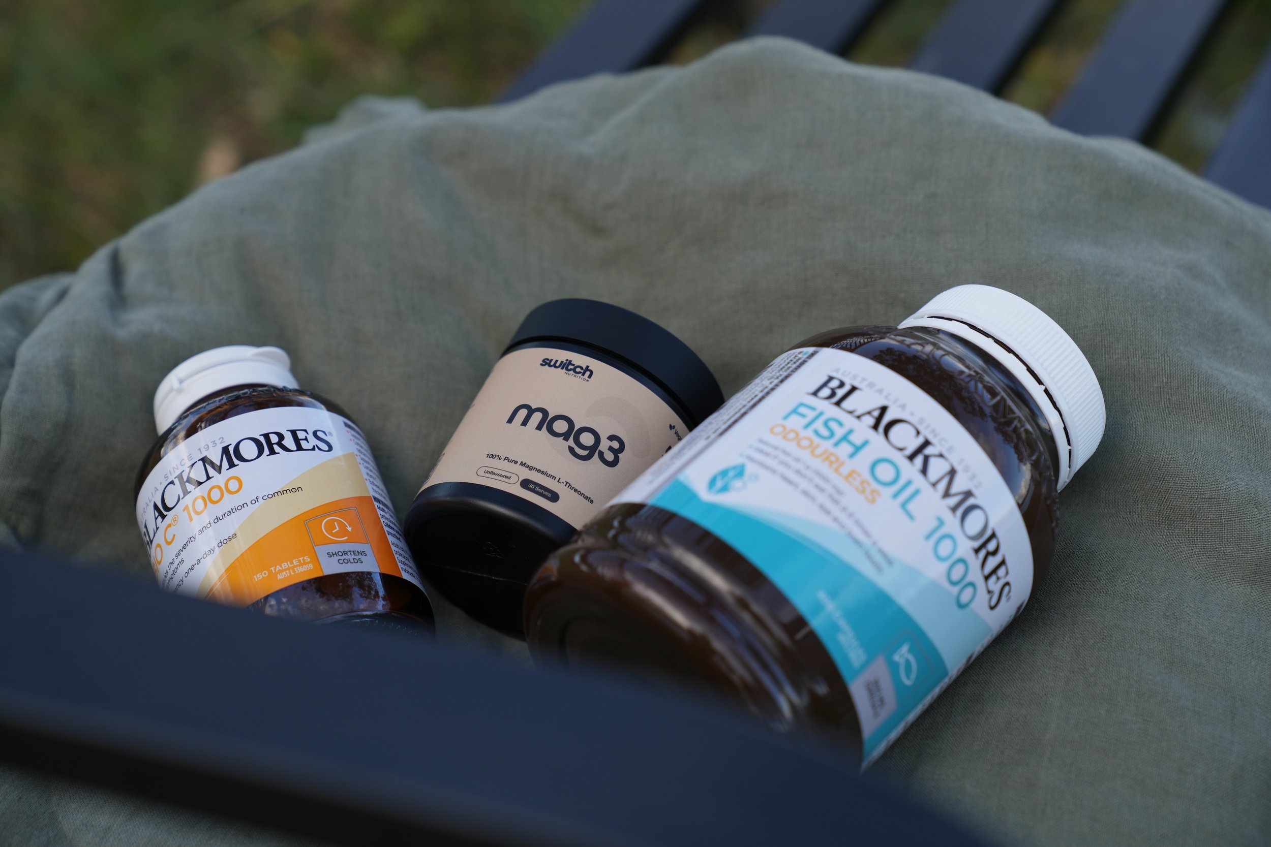 Three bottles of dietary supplements resting on a person's lap outdoors, with a blurred background of greenery.