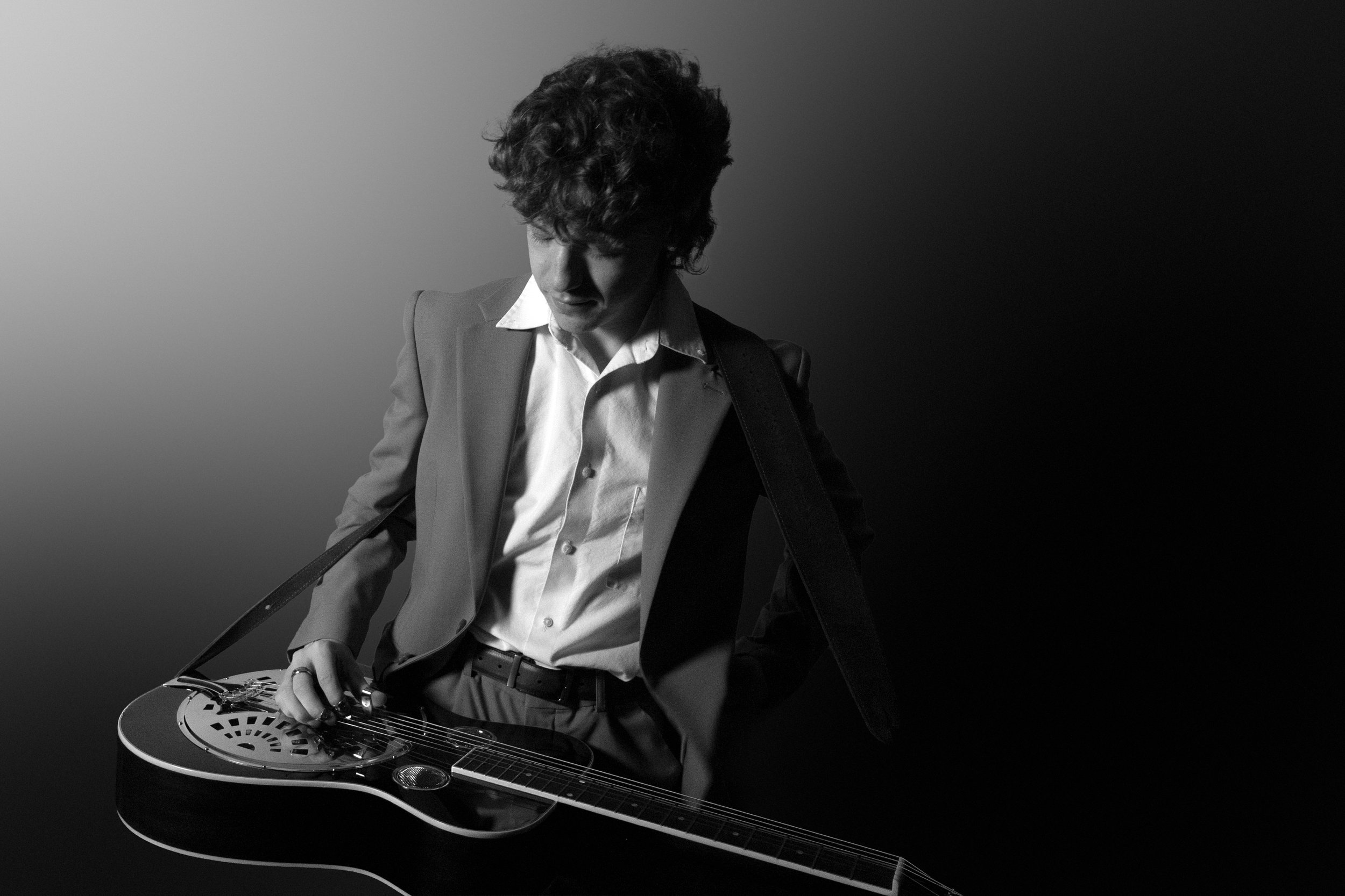 A man in a suit playing an electric guitar against a split shadowed background, black and white photograph.