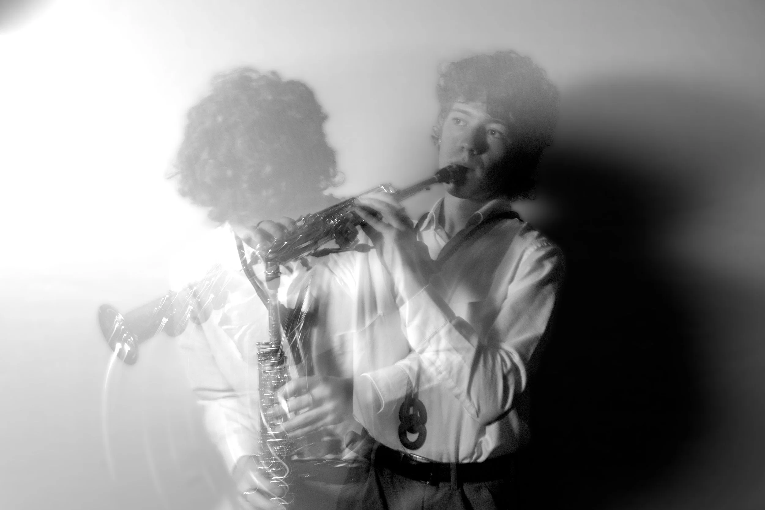 A young man playing a wind instrument, possibly a flute or clarinet, with a water bottle and microphone in front of him, in an indoor setting with a plain background.
