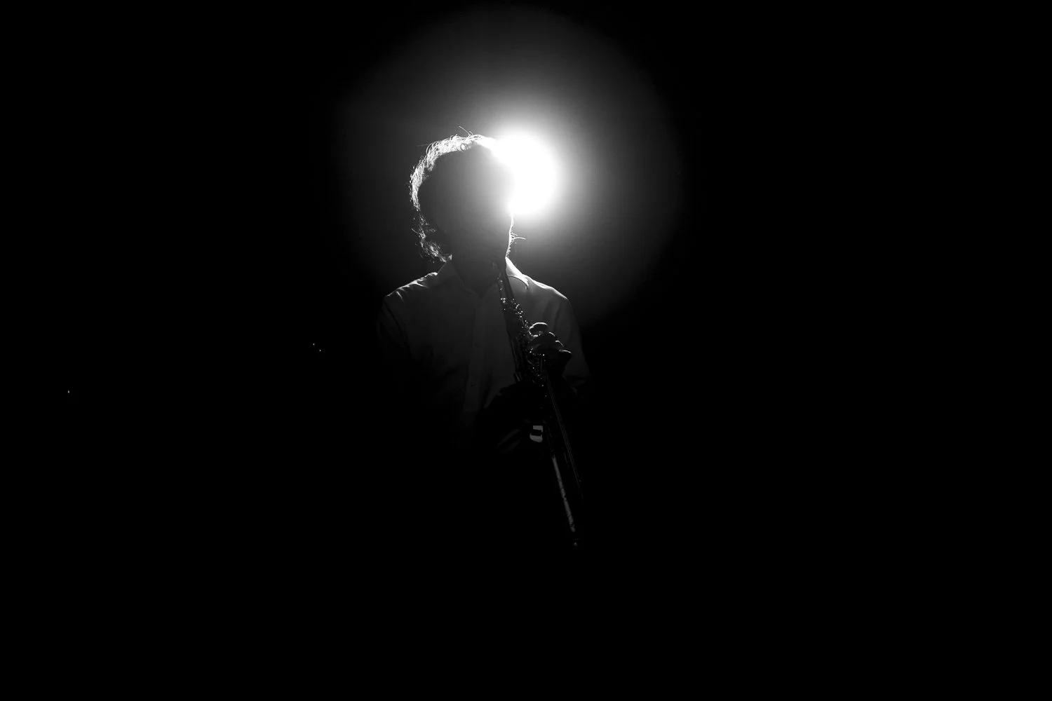 Black and white silhouette of a person playing a flute on stage, backlit with a bright light