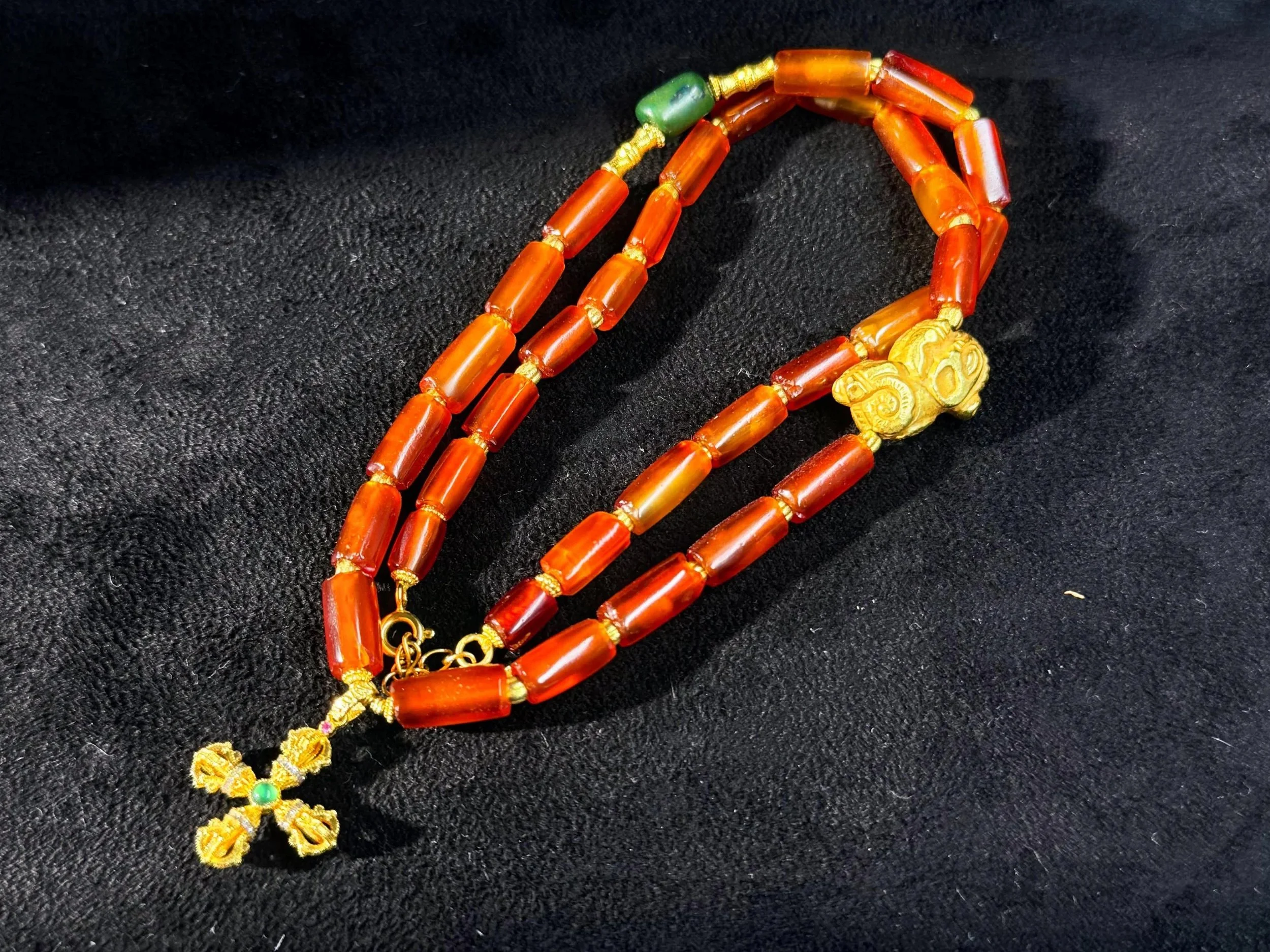Orange and green beaded necklace with a yellow decorative pendant on black fabric background.