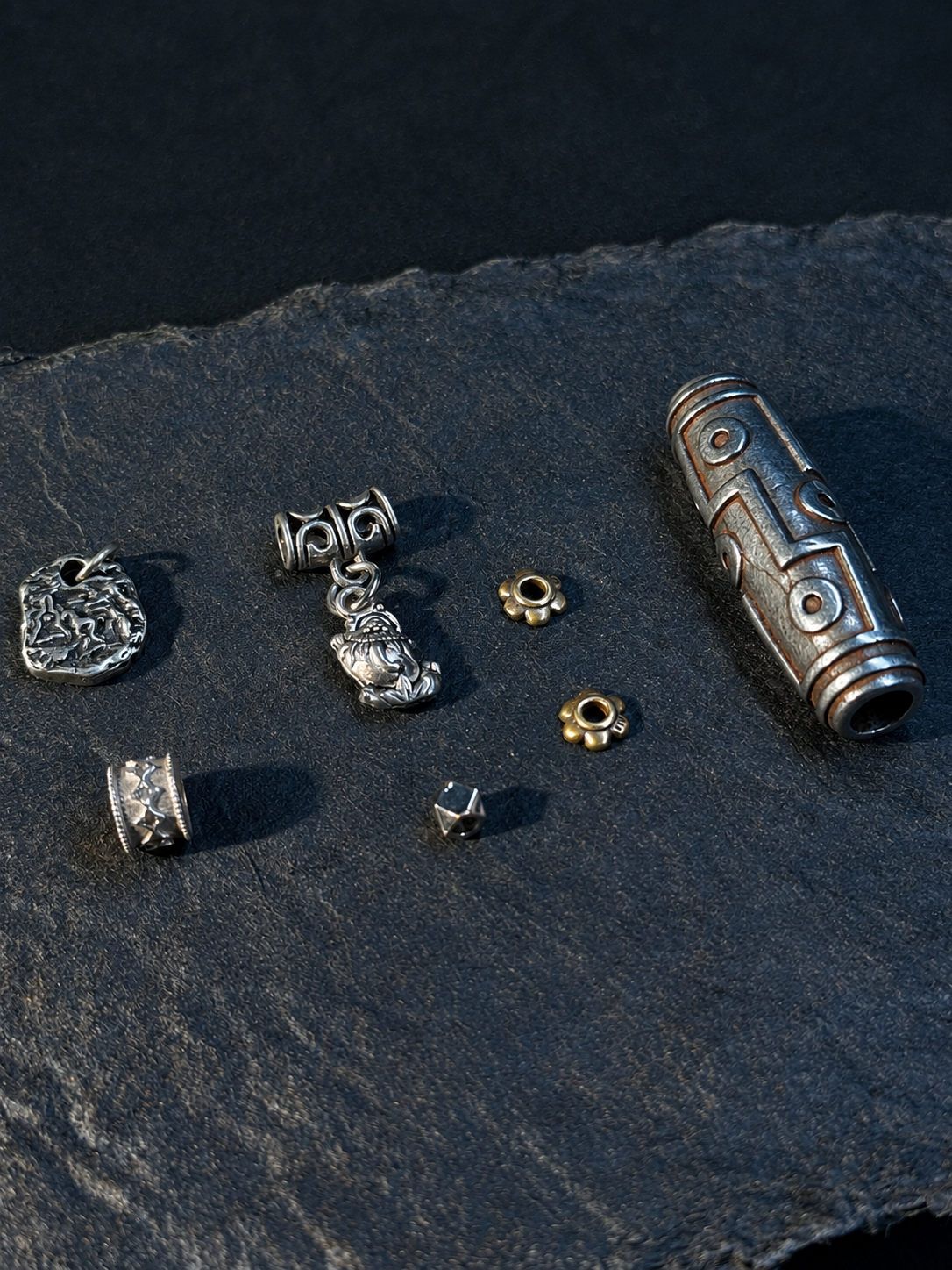 Assorted metallic beads and a carved metallic tube on a dark fabric surface