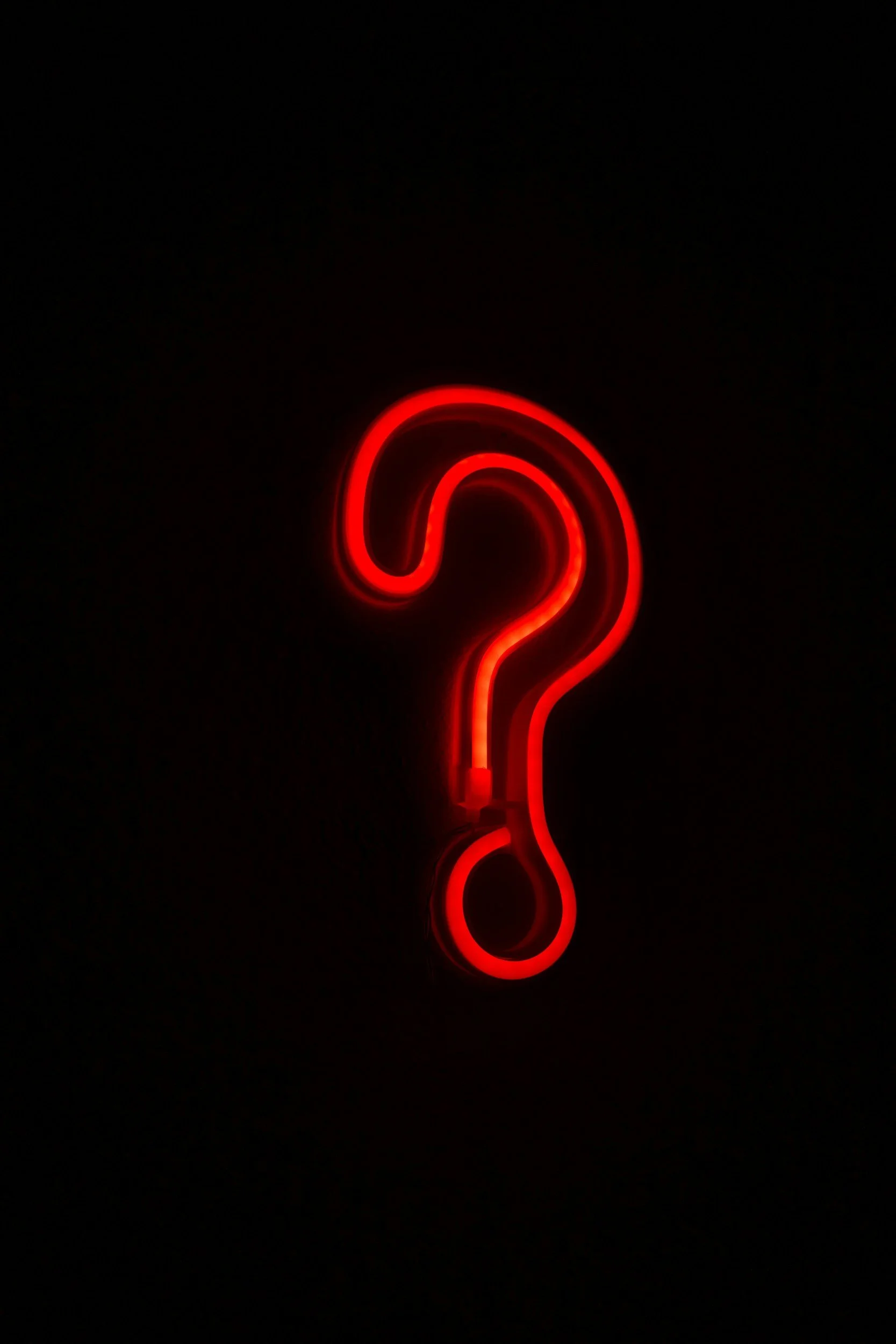 Red neon question mark glowing against a black background.