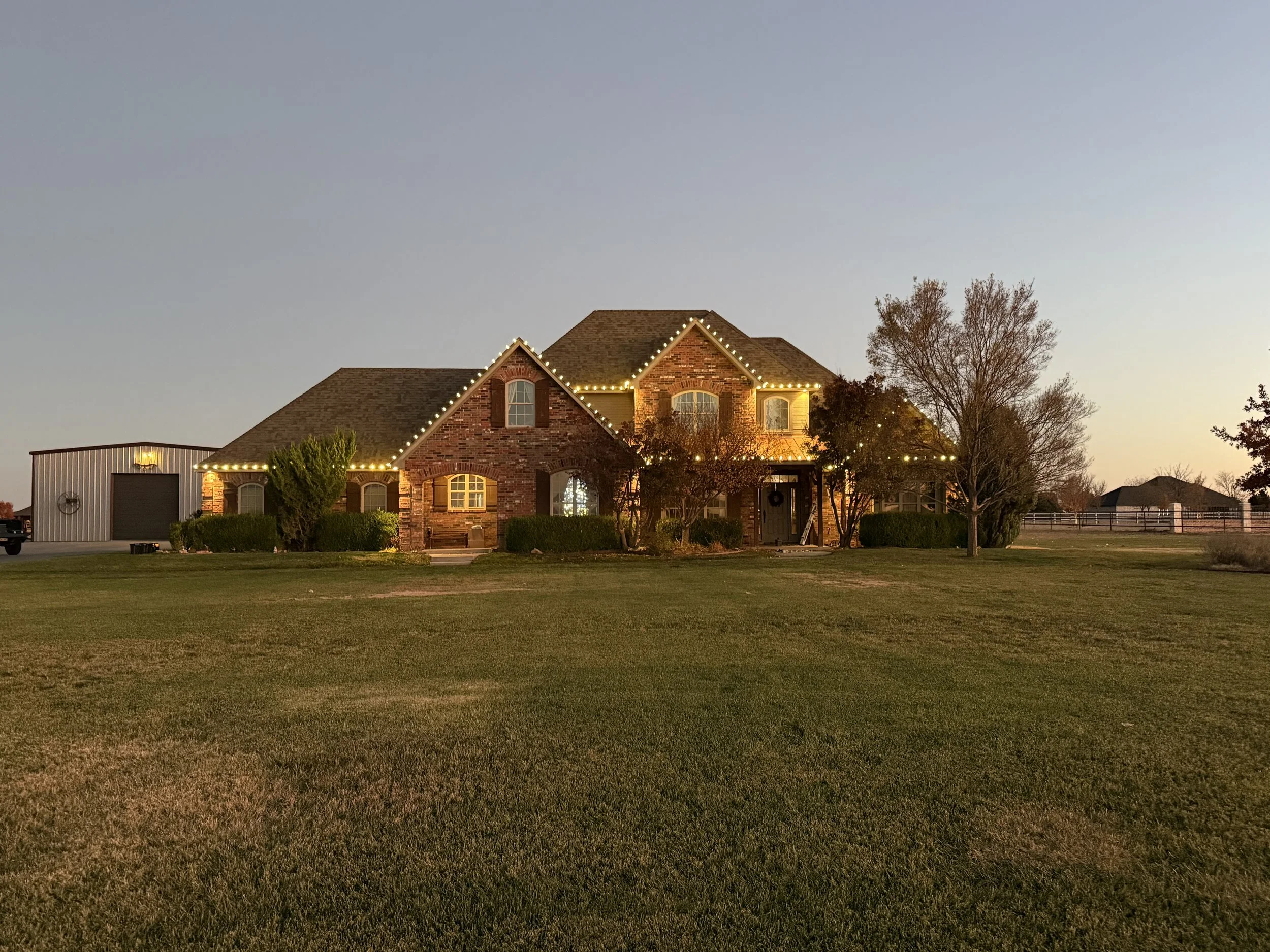 Nighttime view of a brick house with outdoor lights, surrounded by a lawn and trees.