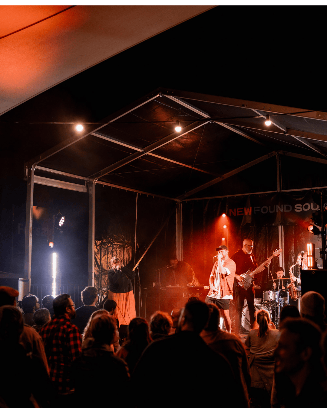 A live music performance on stage with a band and singer, audience watching, stage lights in a concert setting.