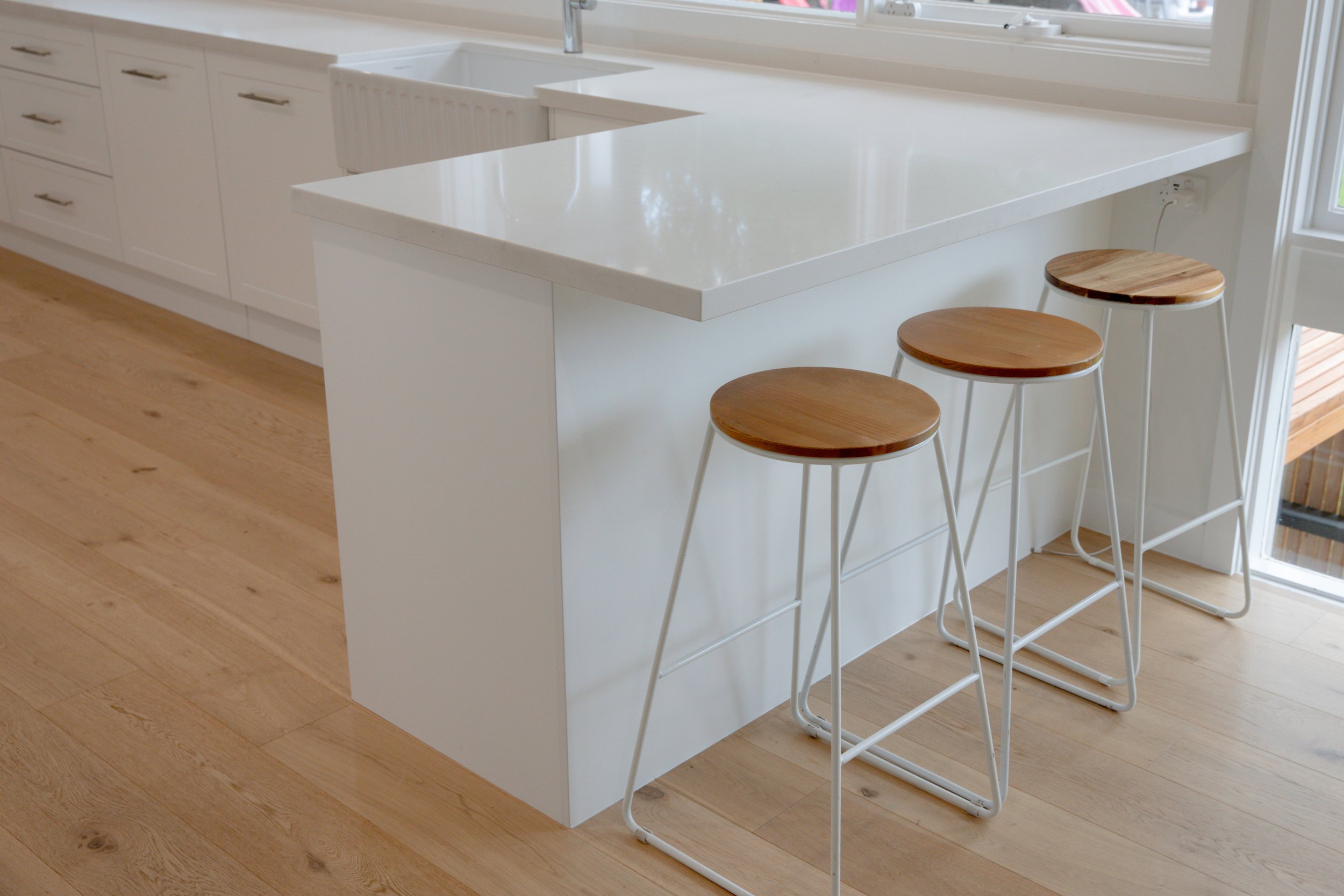 White kitchen island with wooden bar stools, white cabinets, hardwood flooring, and a window.