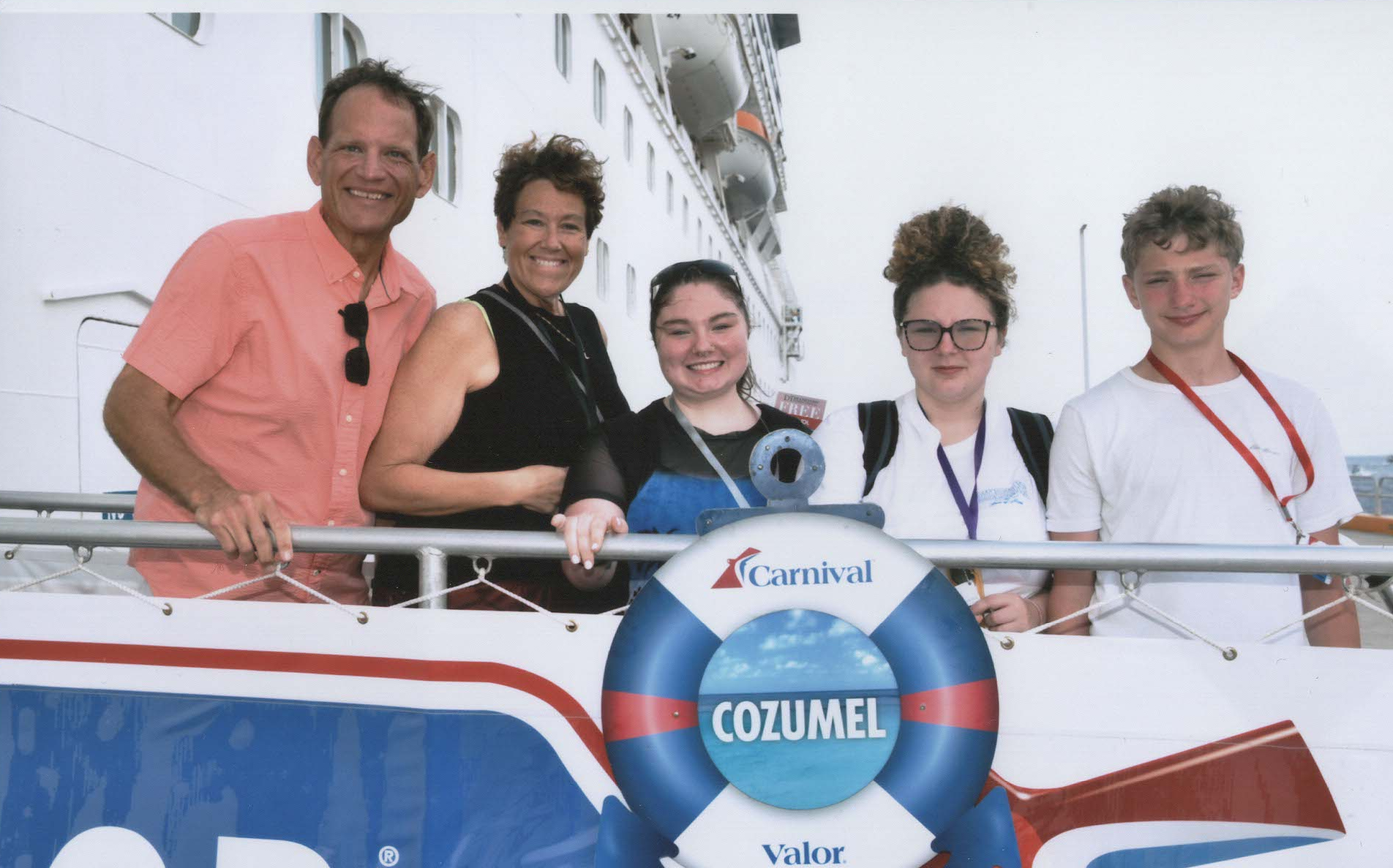 Group of five people smiling on a ship's deck, with a life preserver that says "Cozumel" and the Carnival logo, in Cozumel, Mexico.