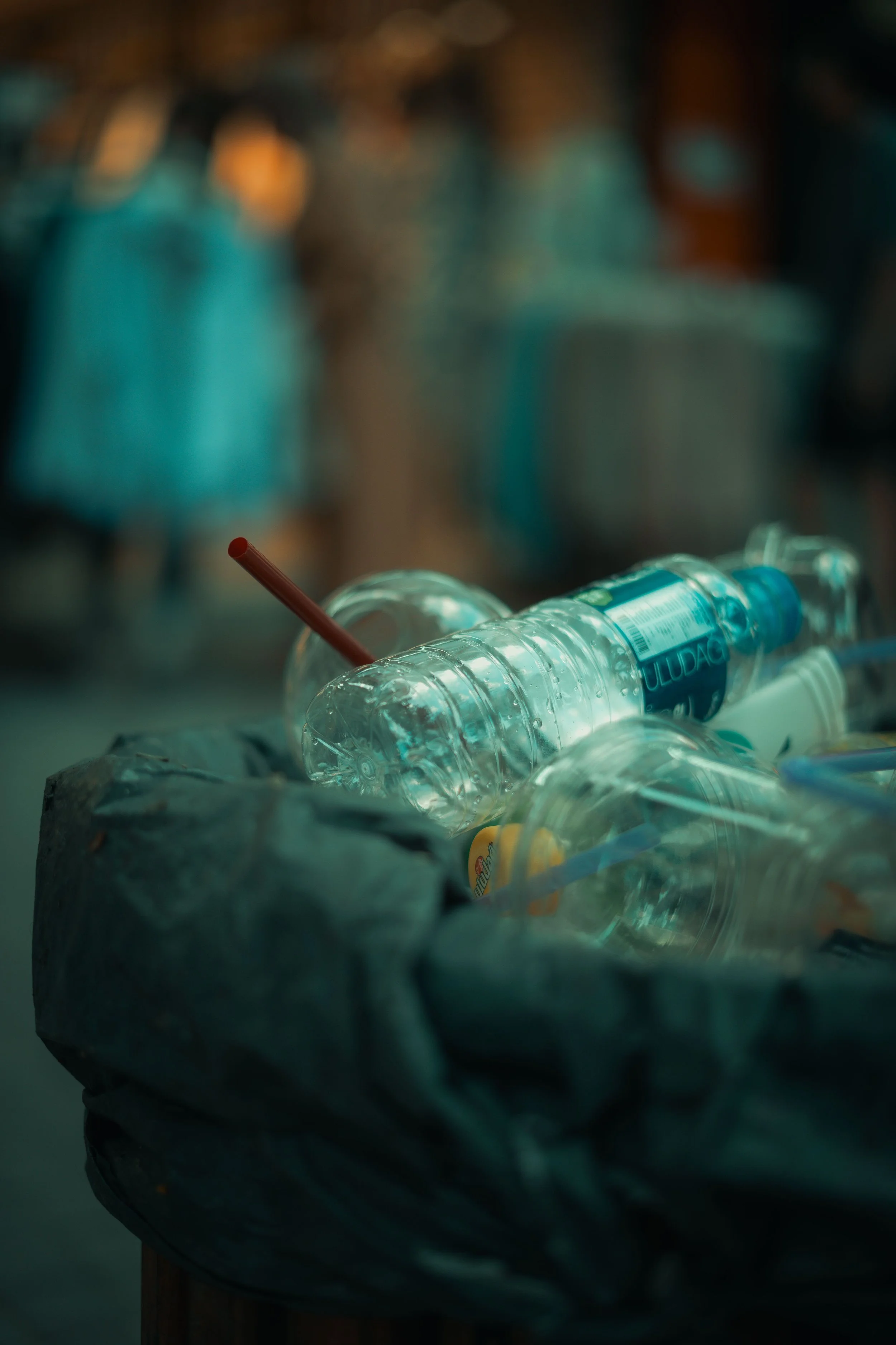 A pile of crumpled trash containing plastic bottles, with a background of blurred people.
