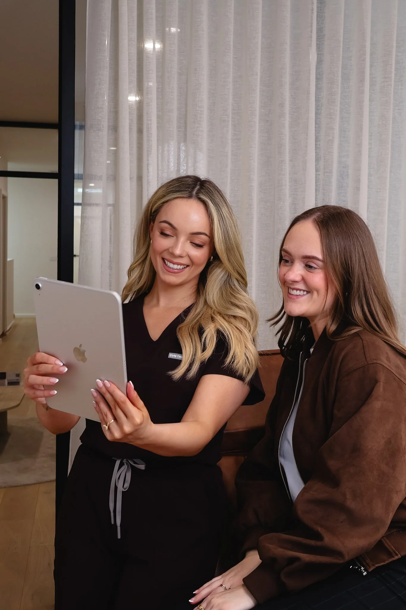 Two smiling women looking at a tablet device together in a cozy indoor setting.