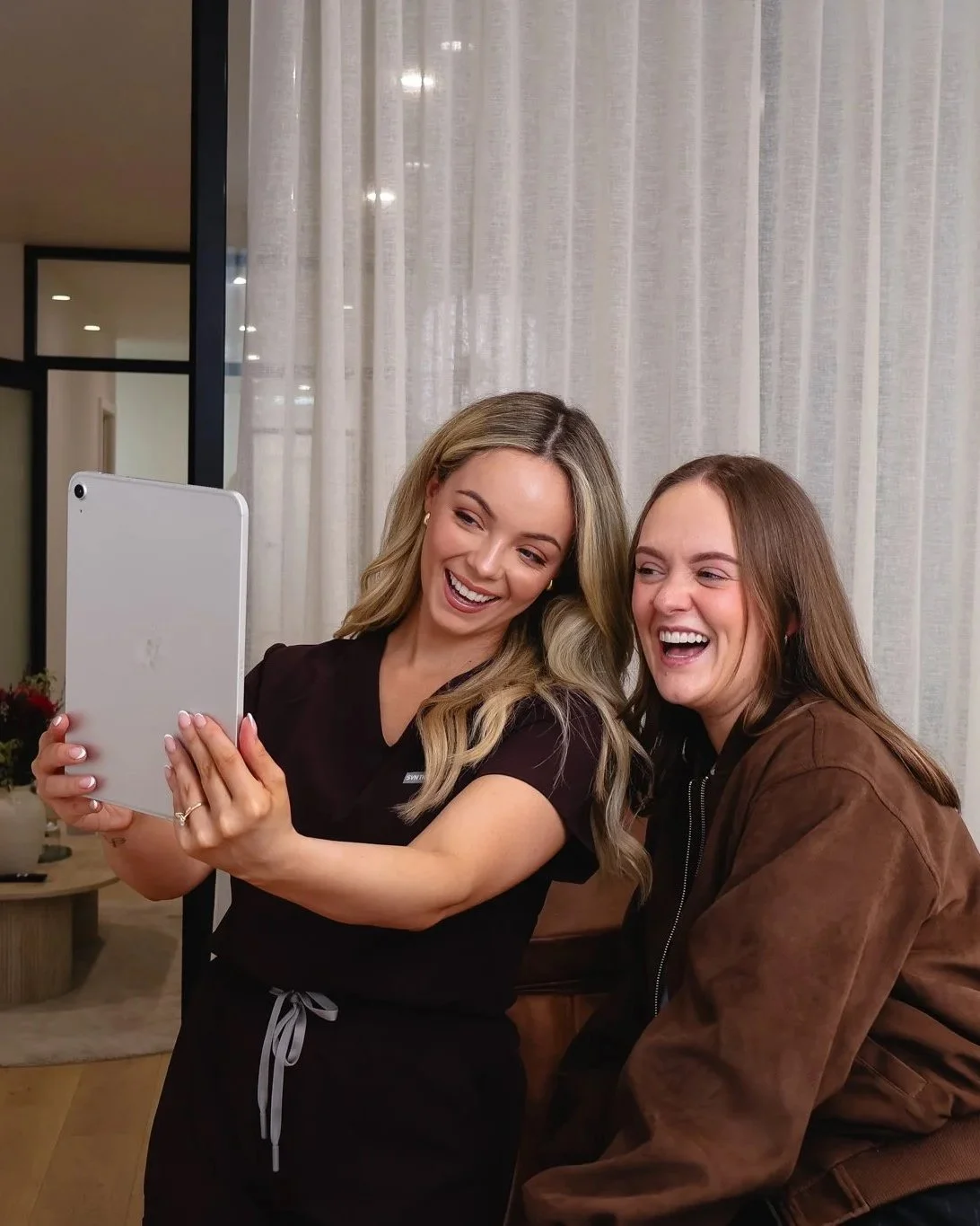 Two women smiling and taking a selfie together in a cozy indoor setting.