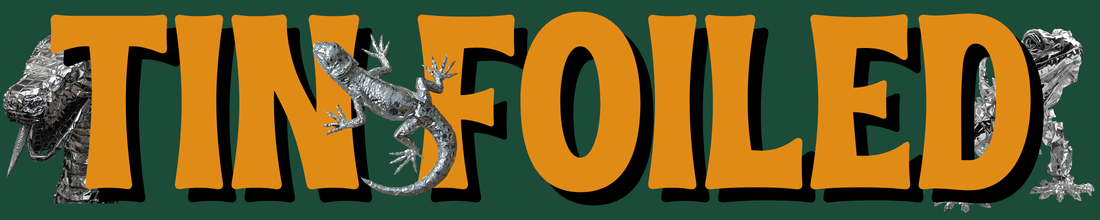 Text says 'TINS FOILED' with a lizard and snakes made of crumpled aluminum foil integrated into the letters on a dark background.