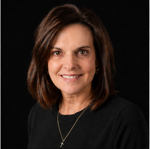 A middle-aged woman with shoulder-length brown hair, wearing a black top, a gold cross necklace, and gold earrings, smiling at the camera against a black background.