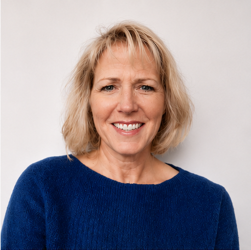 A middle-aged woman with blonde, wavy hair smiling and wearing a blue sweater against a plain white background.
