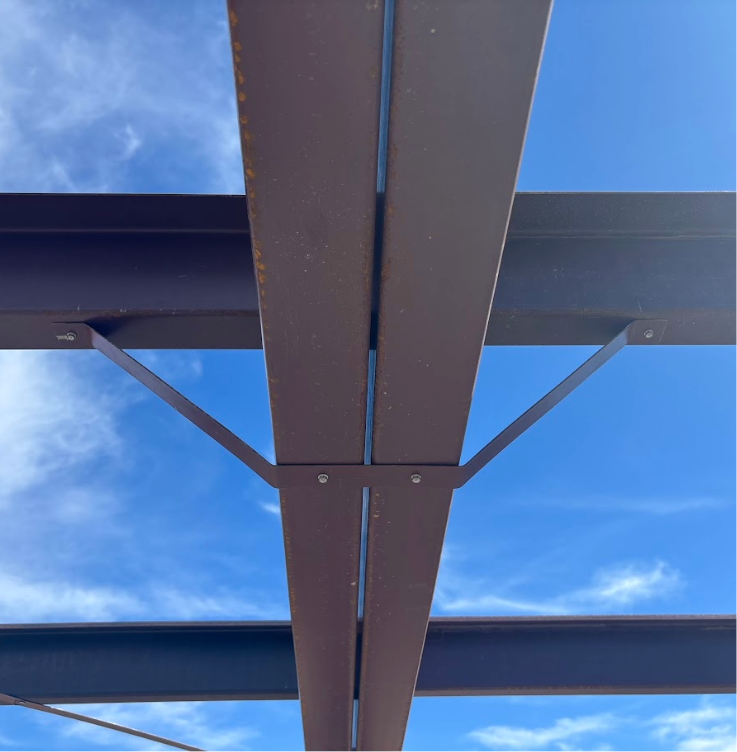 Close-up view of a steel rafters with fly bracing against a clear blue sky with some clouds.