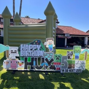 Minecraft-themed birthday party decorations with a colorful banner reading 'Happy Birthday Jax' and various Minecraft characters and blocks on a lawn.