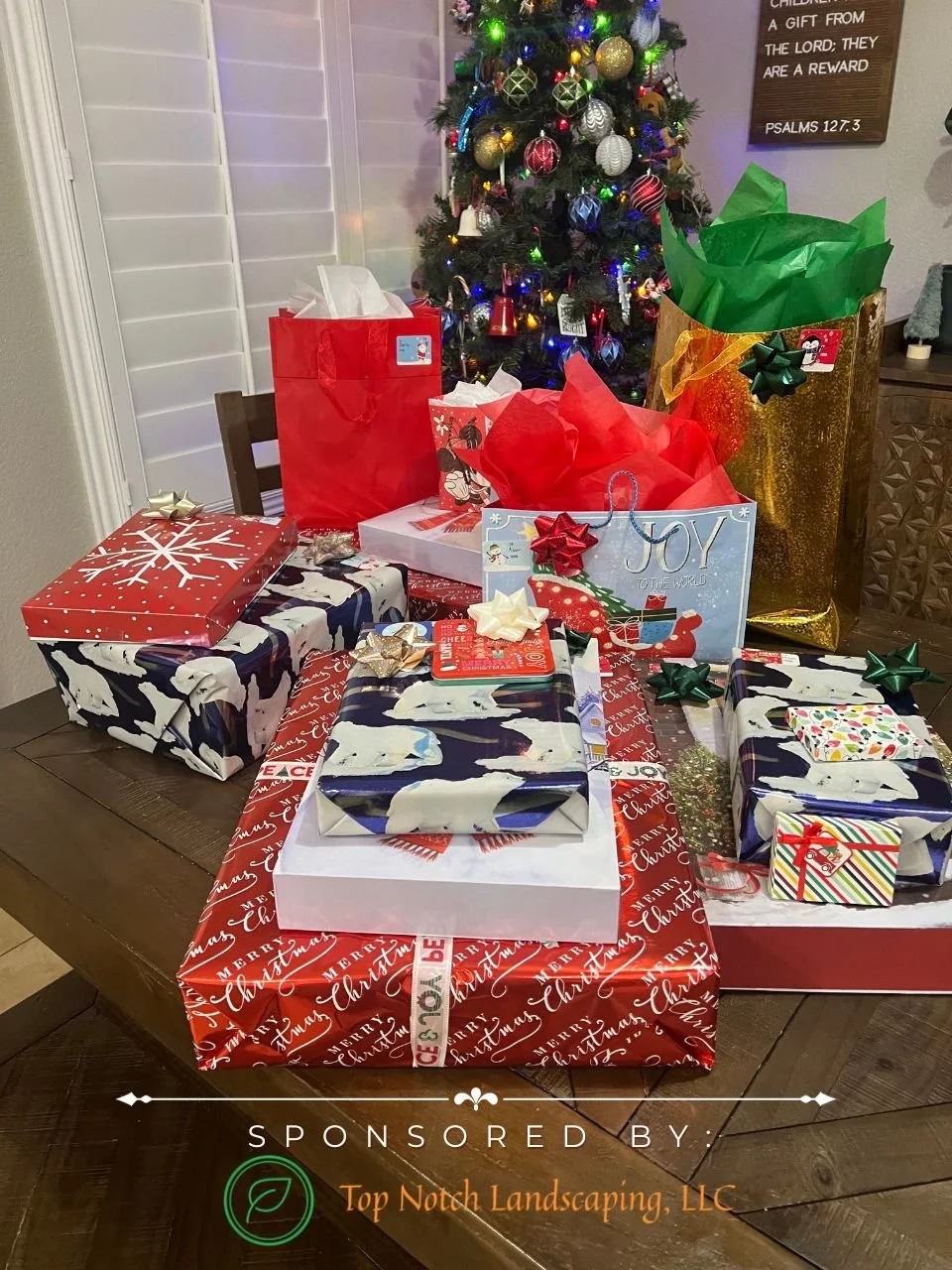 Christmas presents under a decorated Christmas tree, including wrapped gifts with festive paper and bows, and gift bags, set on a wooden table with a Christmas-themed table runner.