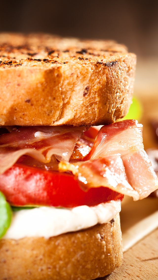 Close-up of a toasted sandwich with layers of bacon, tomato, and cheese