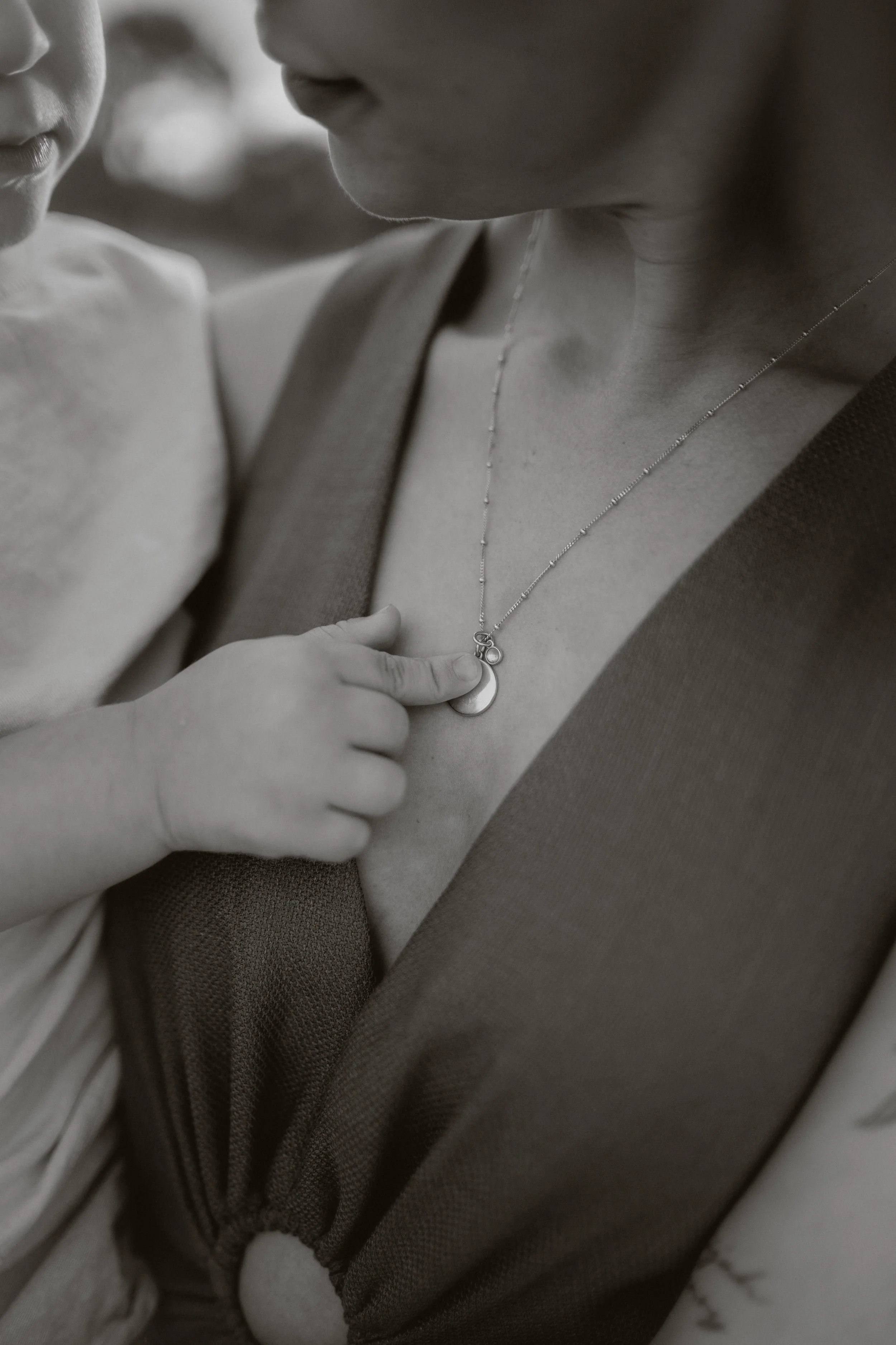 Close-up of two children with a necklace, one child touching the necklace near their collarbone, black-and-white photo.