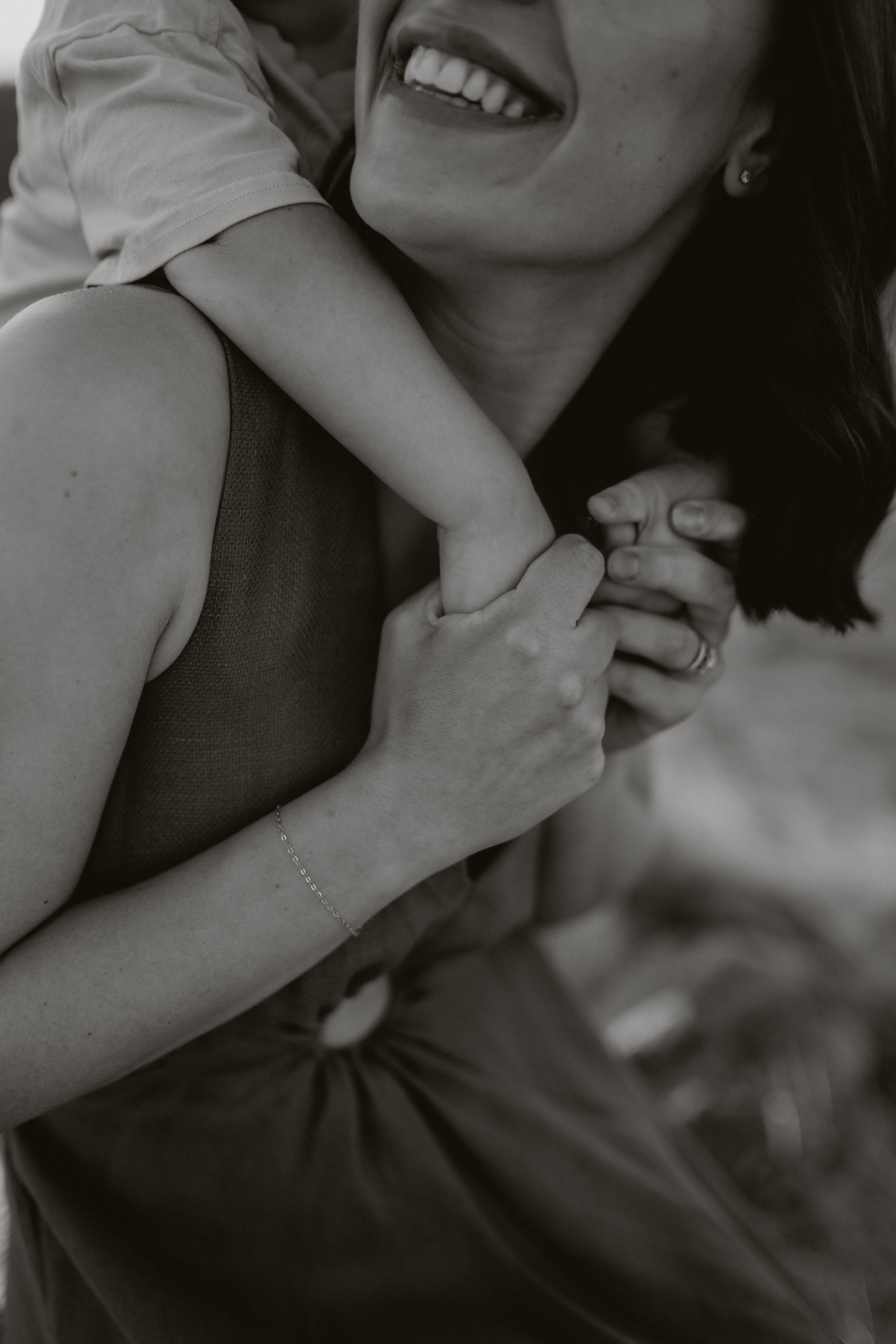 Close-up of a smiling woman holding a child's arm, black and white photo.