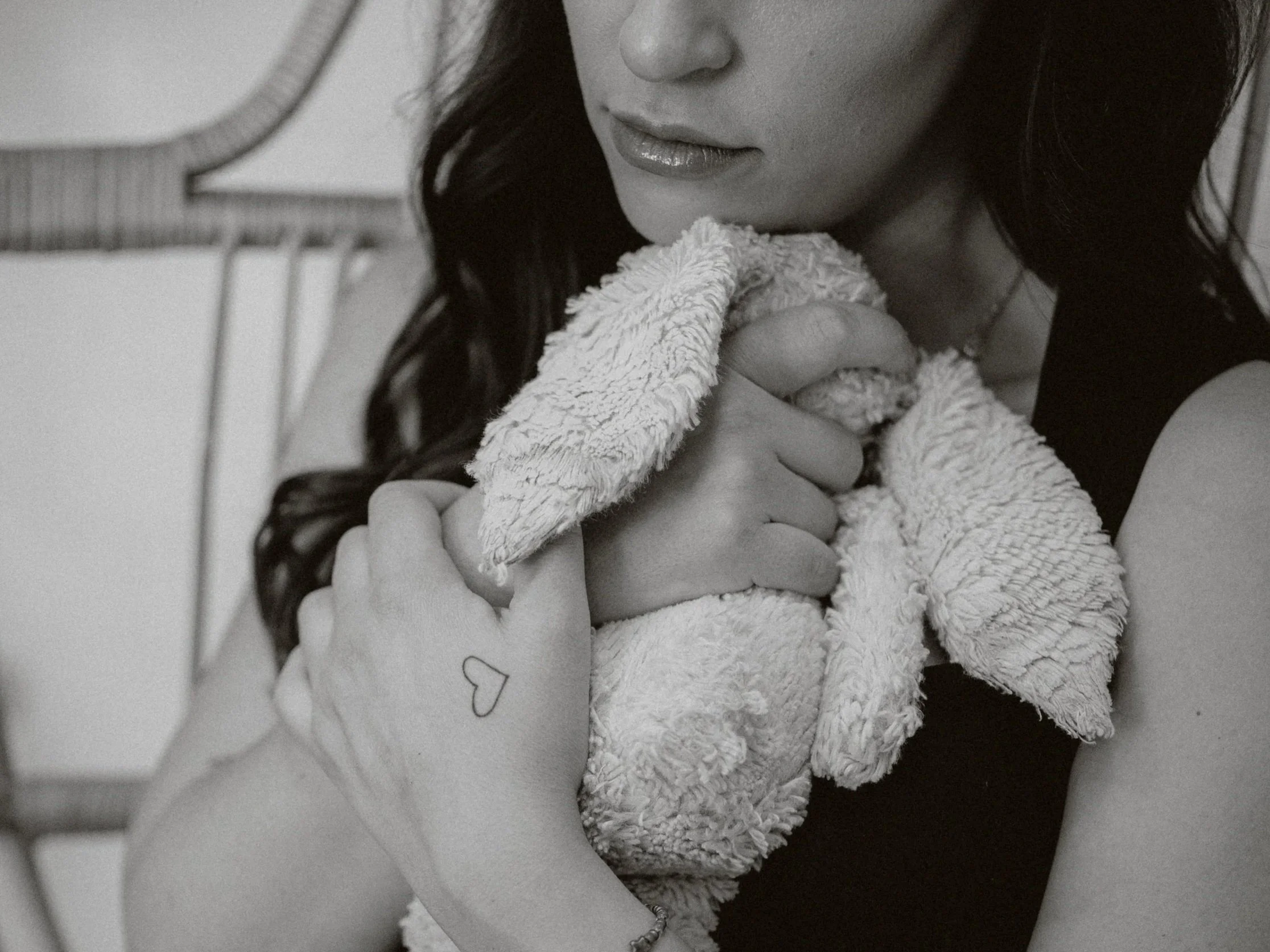A black and white close-up photograph of a woman holding a small fluffy dog. The woman’s face is partially visible, showing her lips and nose. The dog is being held close to her face, and she is gently touching its head.