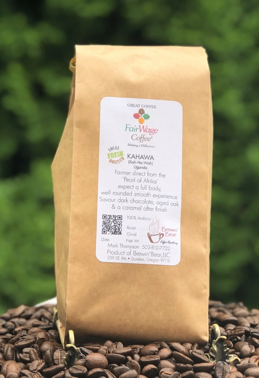 A brown paper bag of FairWage Coffee sitting on coffee beans with a blurred green background.