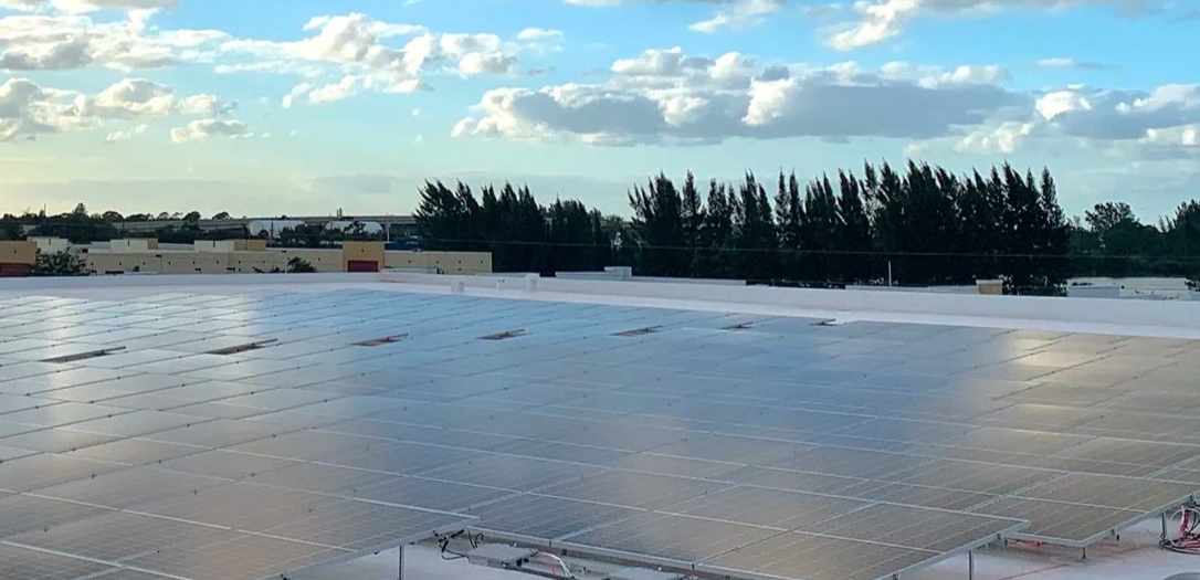 Rooftop solar panels installed on a flat roof with a blue sky and scattered clouds in the background.