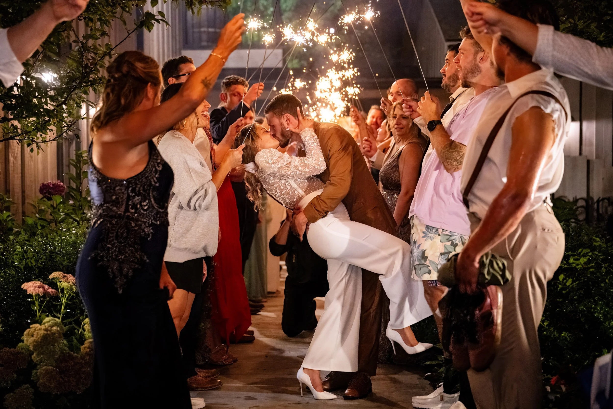 Alt text: Bride and groom walking through a nighttime sparkler exit send-off surrounded by wedding guests at Stonehurst at Hampton Valley in Connecticut. Photographed by Allison Mott of Mott Collective.