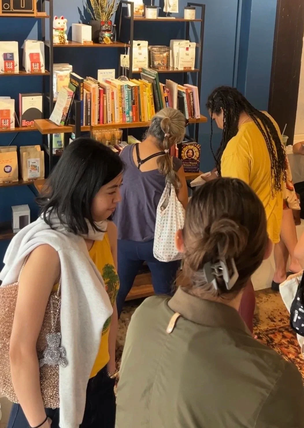 People browsing books in a bookstore with blue walls and shelves filled with books and decorative items.