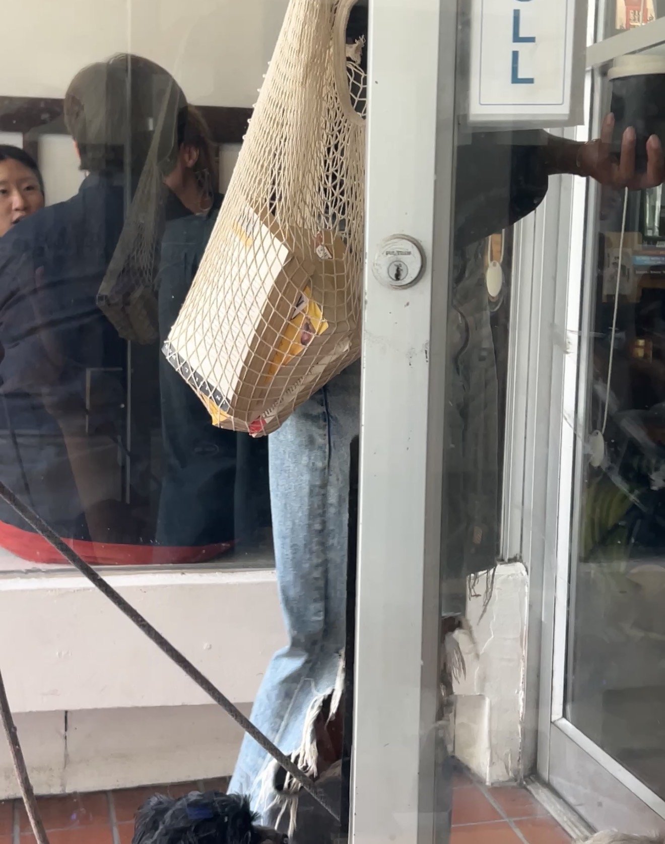 People standing outside a store behind a glass door, with one person holding a paper bag and others looking in.
