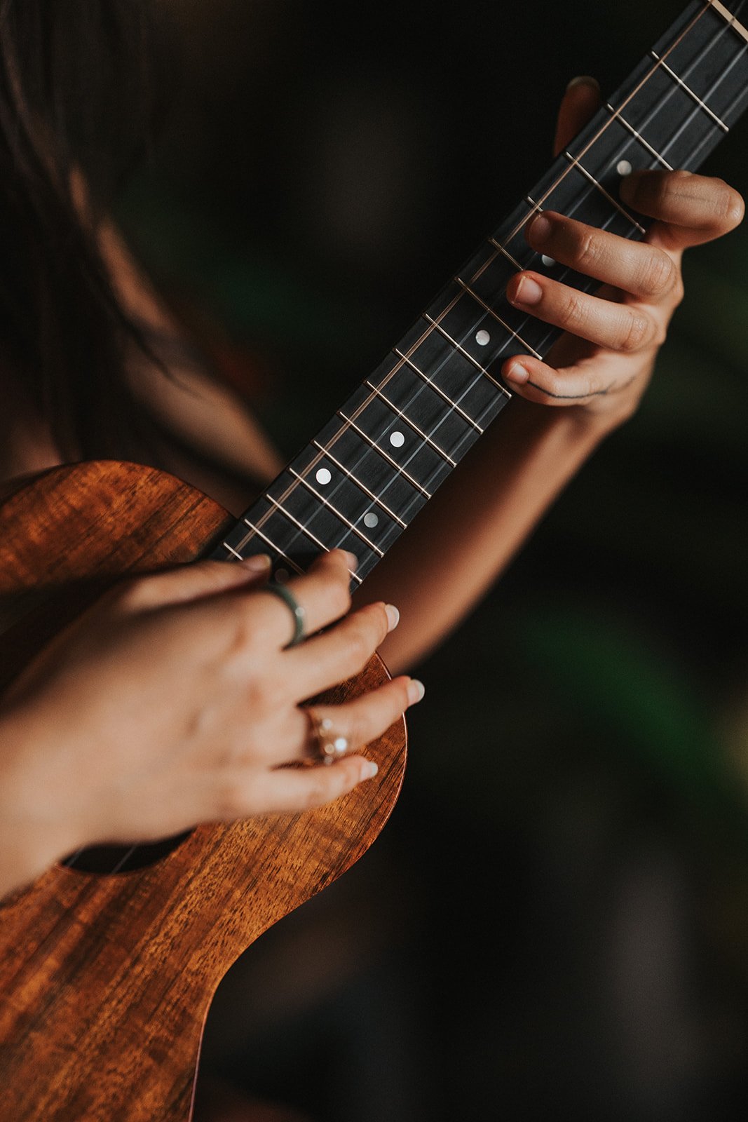 Close-up of a person's hands playing a wooden ukulele with a dark fretboard.