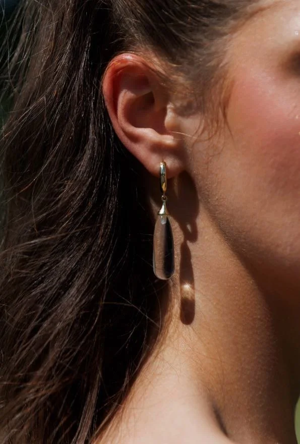Close-up of a woman's ear wearing a gold drop earring with a teardrop-shaped pendant.