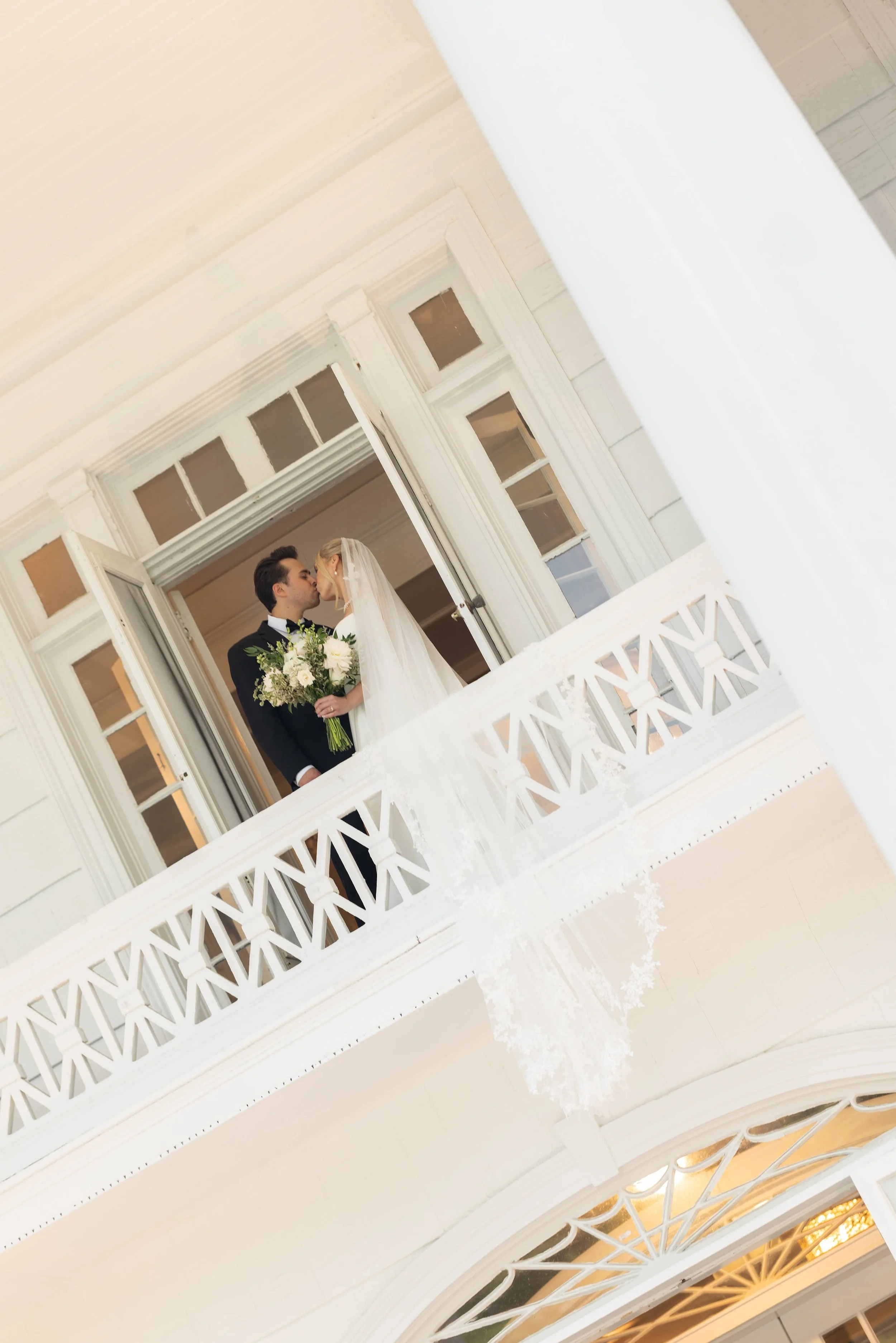 A bride and groom sharing a kiss on a balcony at a wedding.