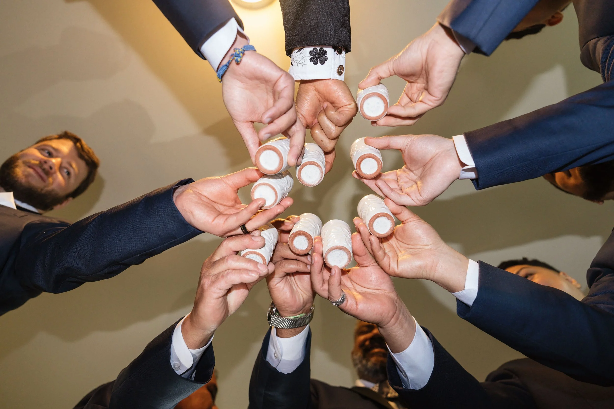 Multiple people in formal suits with dressed-up sleeves is a tight shot, forming a circle with their hands and holding pens.