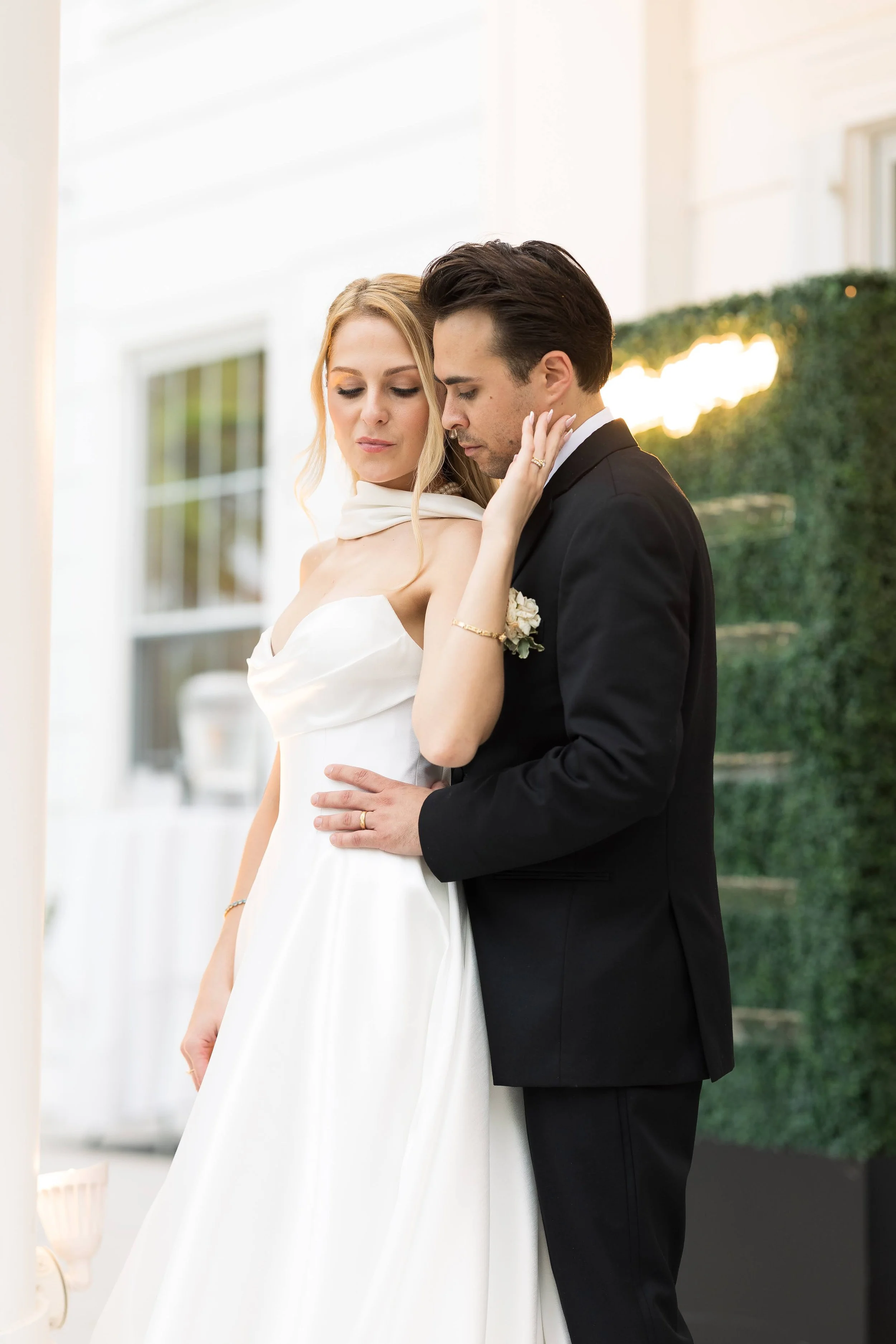 Bride and groom sharing an intimate moment at their wedding, standing close with eyes closed, with a lush green backdrop.