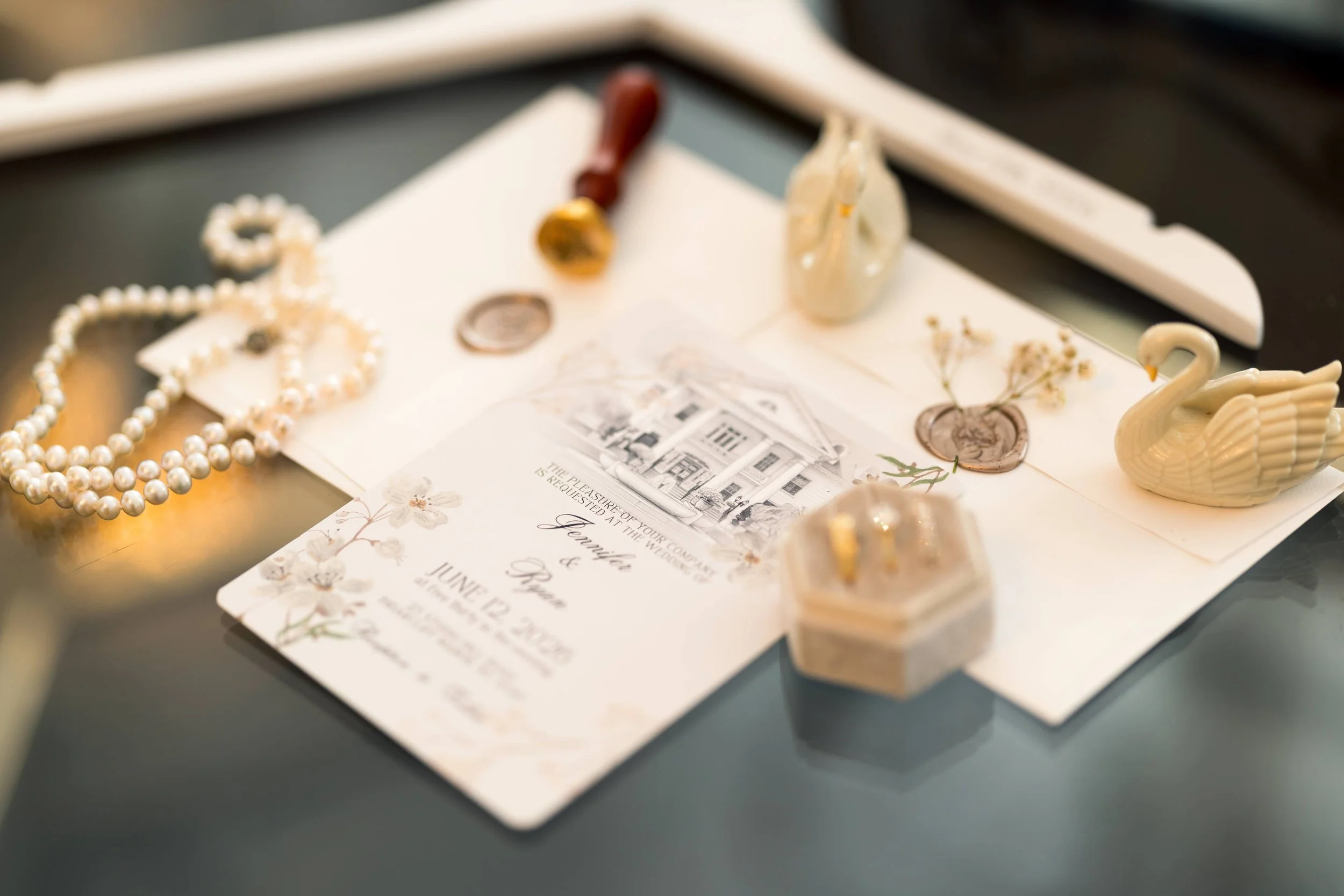 A wedding invitation surrounded by pearls, a swan figurine, dried flowers, and decorative items on a table.