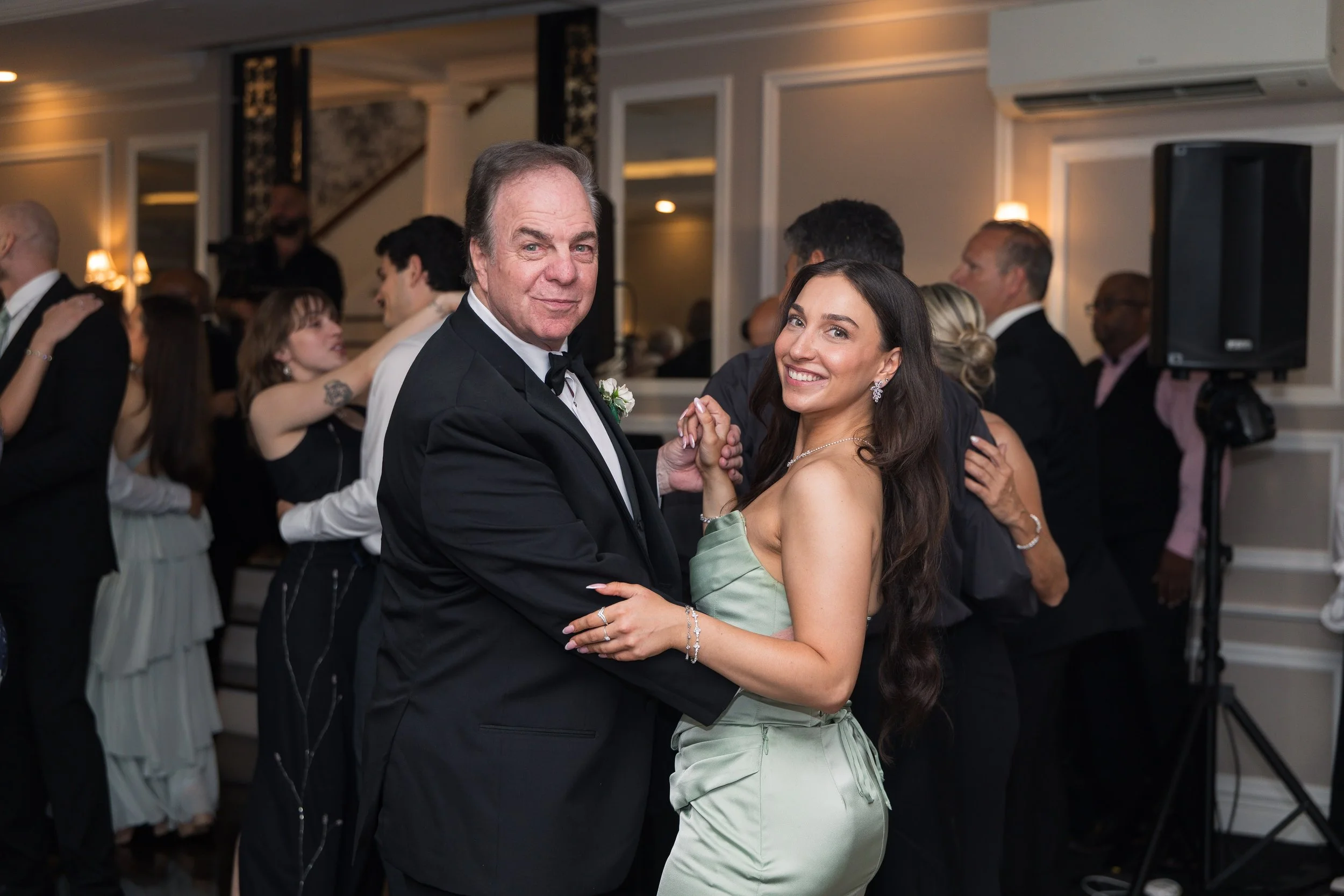 A man and woman dancing closely at a formal event, surrounded by other couples dancing in a decorated ballroom.
